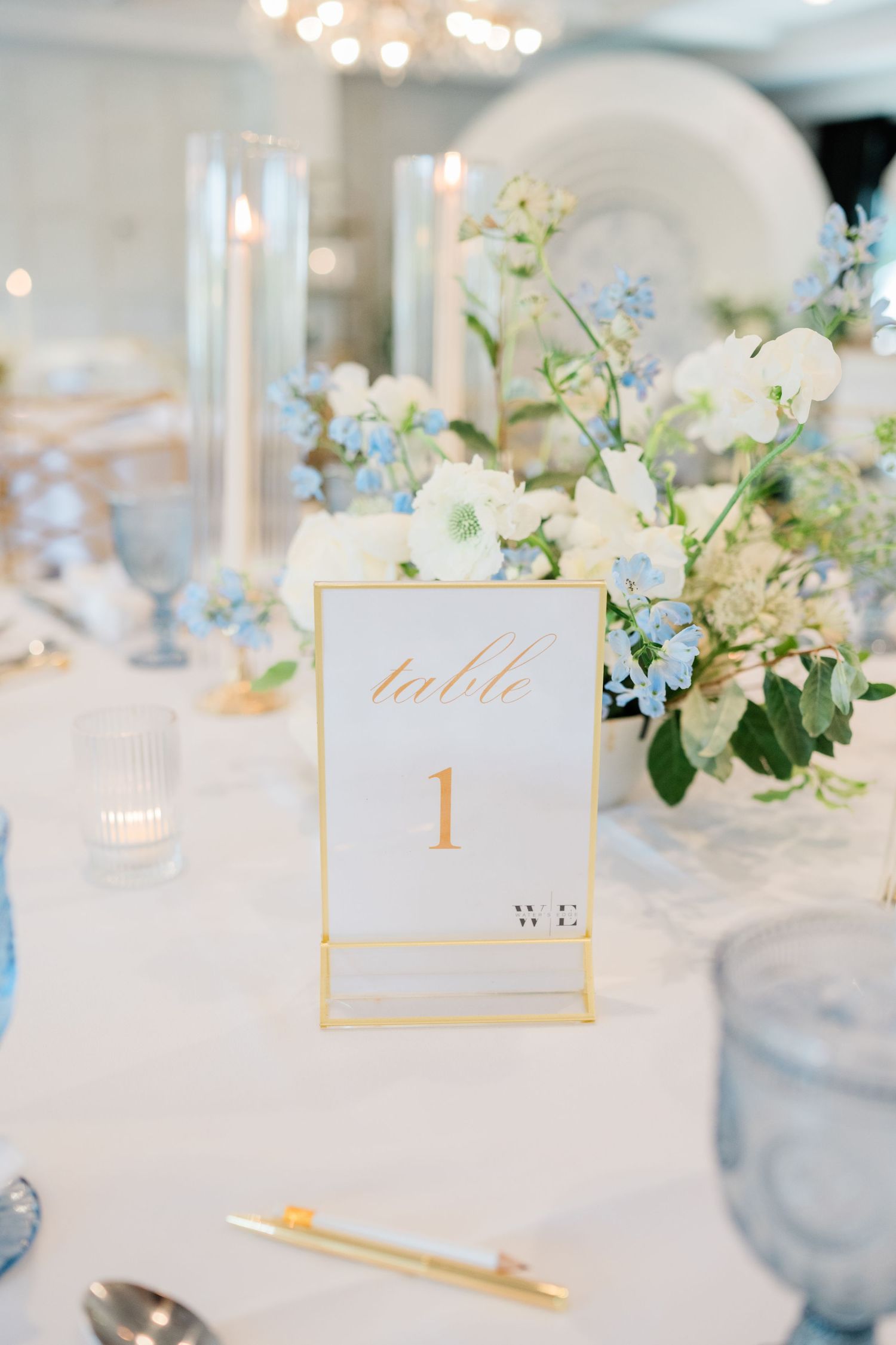 Elegant wedding table settings with delicate floral arrangements and gold-framed table numbers on white linens.