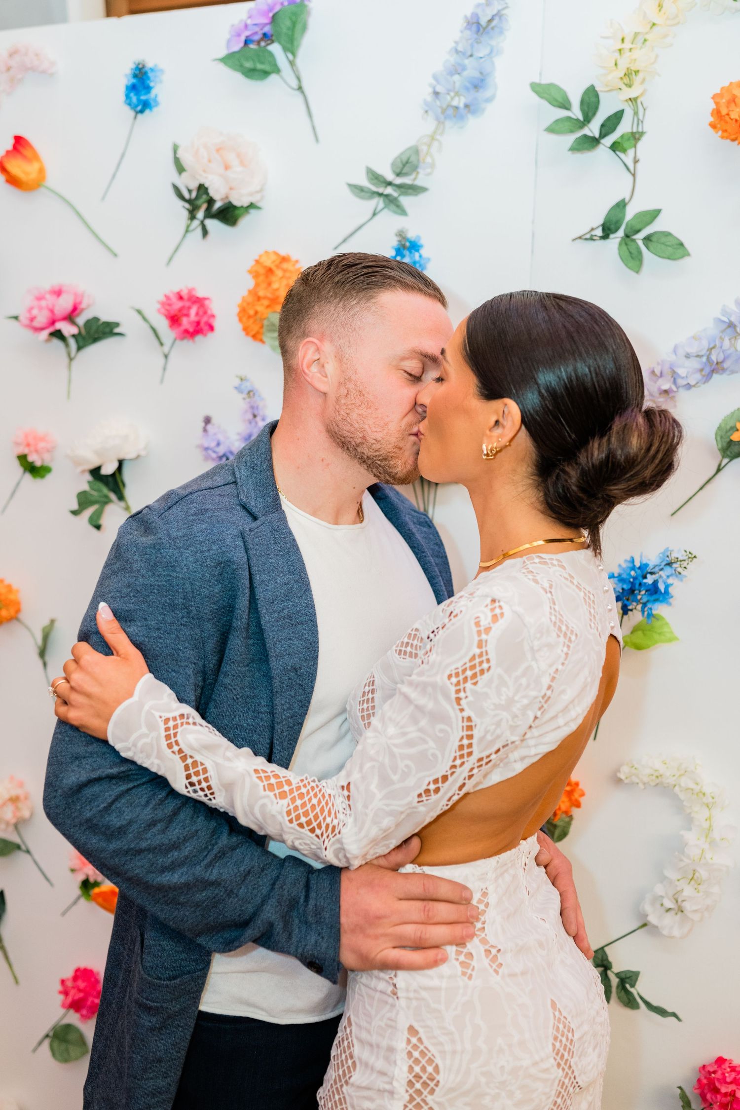 Romantic photoshoot against a floral wall backdrop with scattered colorful blooms.