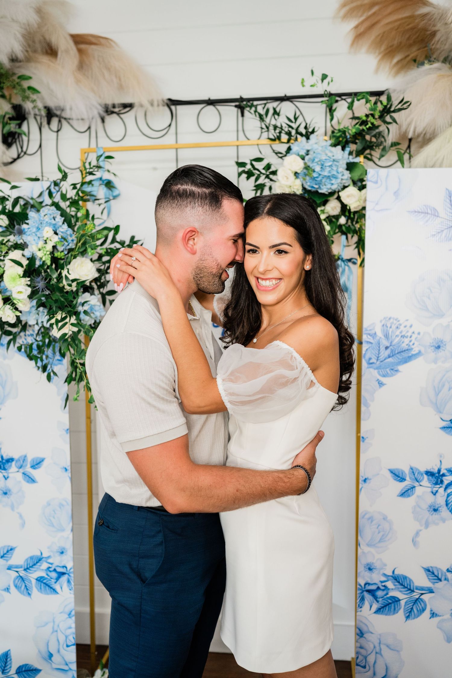 A couple shares intimate moments in front of a blue floral backdrop during a romantic photoshoot.