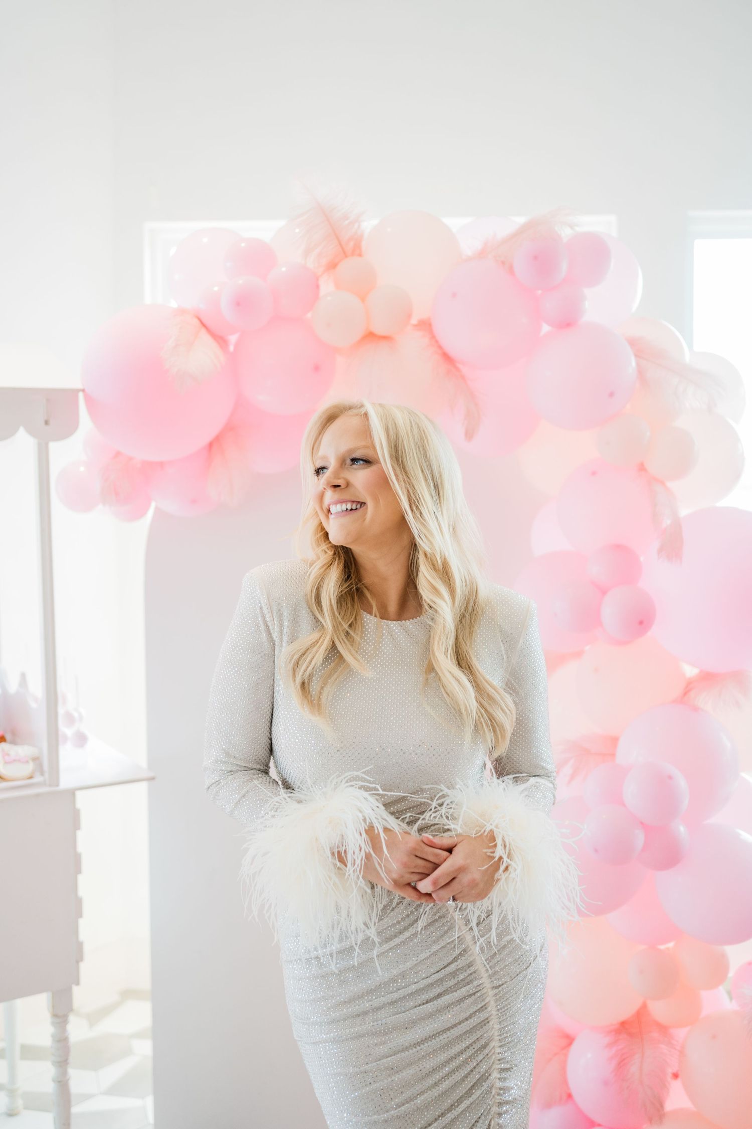Maternity photoshoot with pink balloon arch and white backdrop.