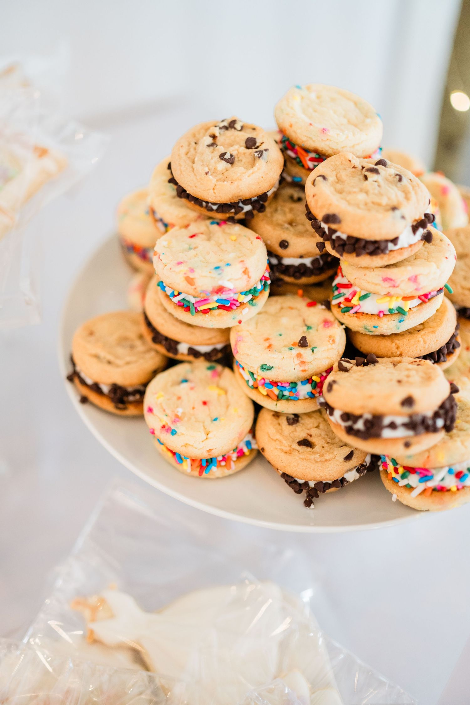 Colorful cookie sandwiches with sprinkles and chocolate filling arranged on white plates.