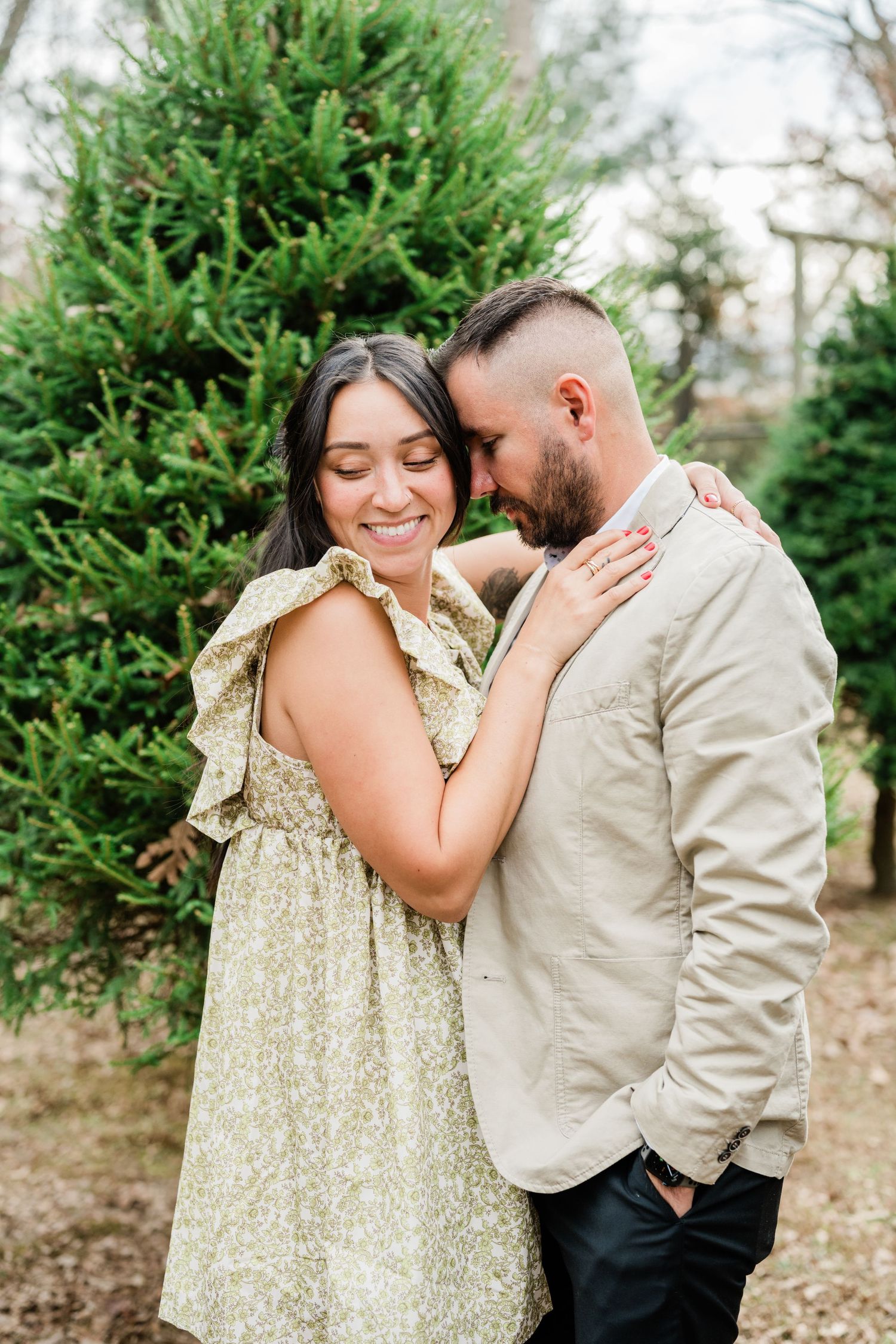 Intimate moment between couple in matching neutral outfits against evergreen tree backdrop.