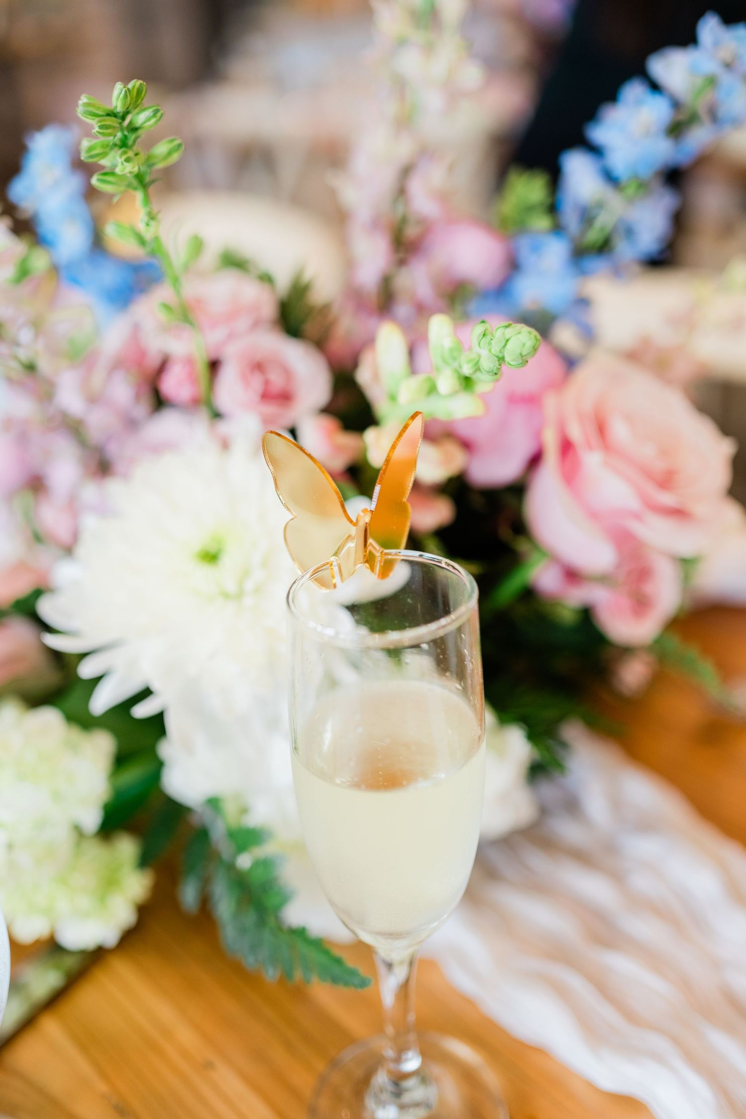 Cocktail glasses garnished with butterflies alongside pink and blue floral arrangements.