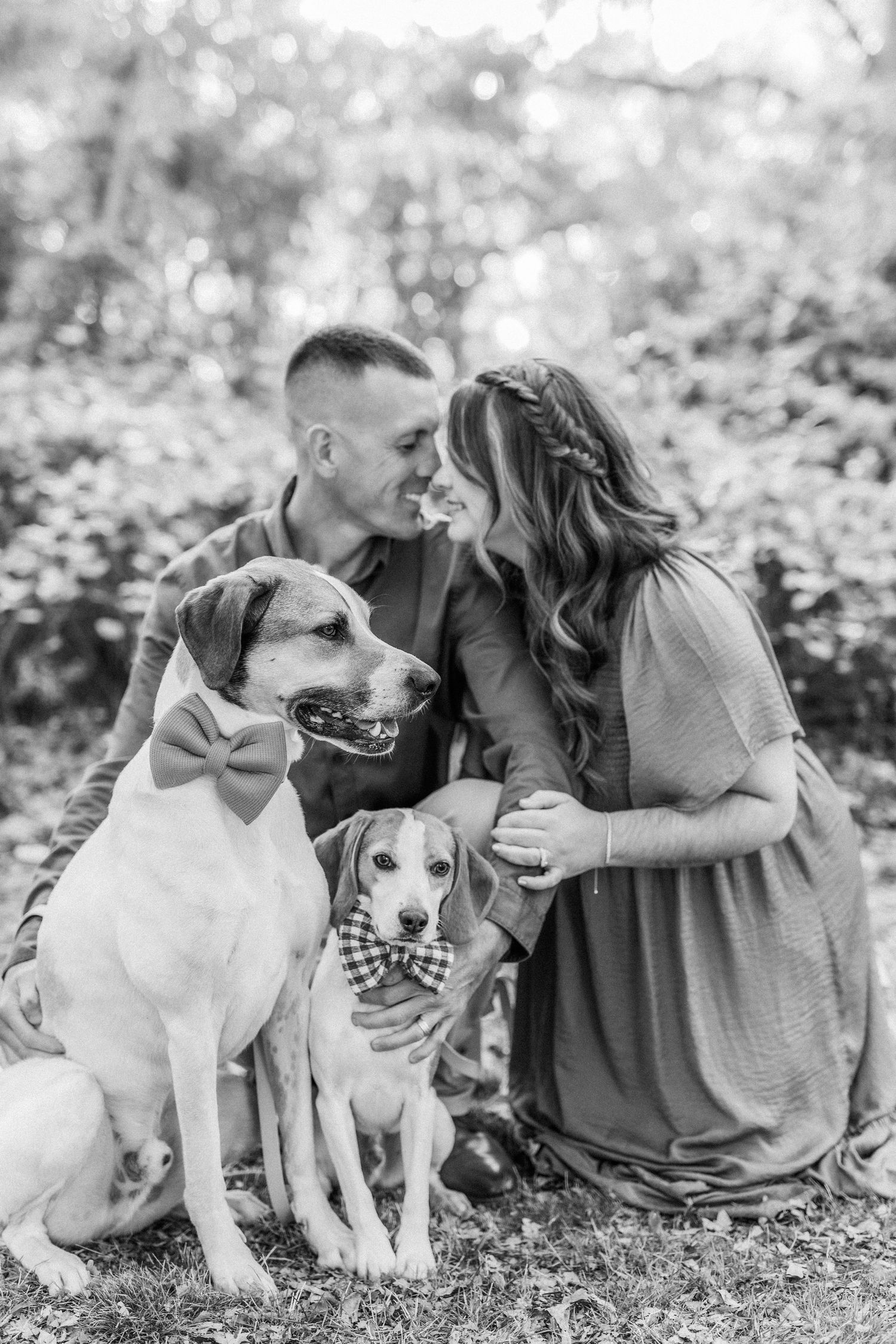 Black and white photo of couple with dogs sitting together outdoors.