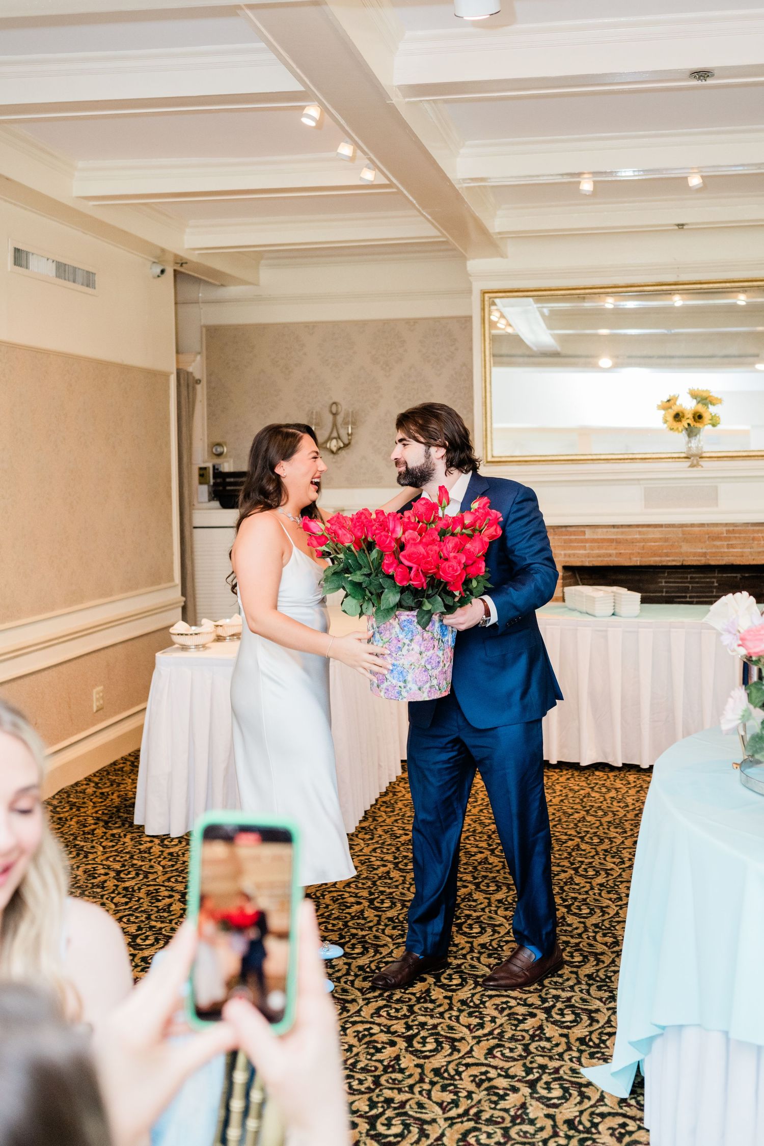 A wedding couple shares a playful first look moment in a reception hall with floral decorations.