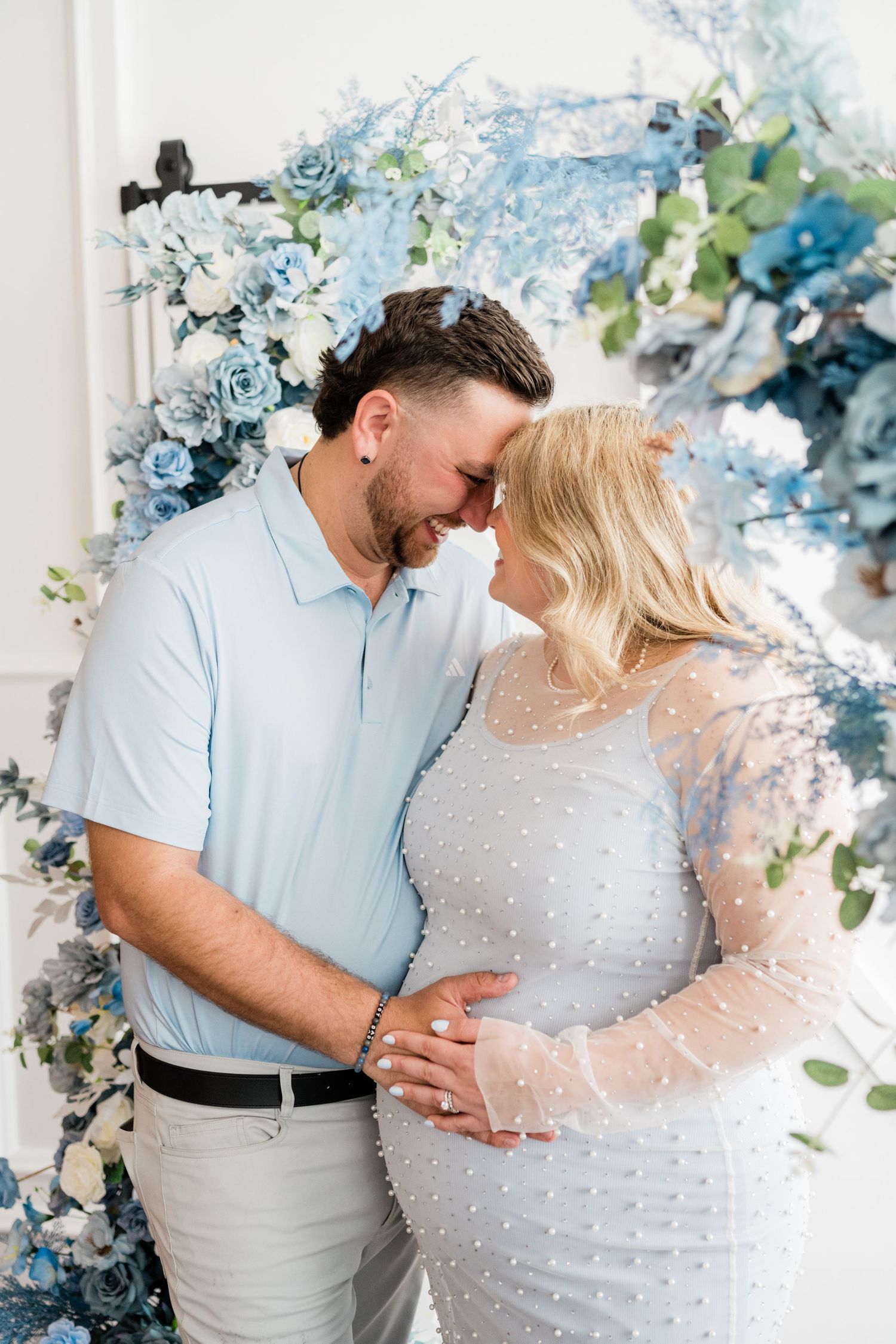 Couple in coordinating blue and white outfits posing against a floral backdrop.