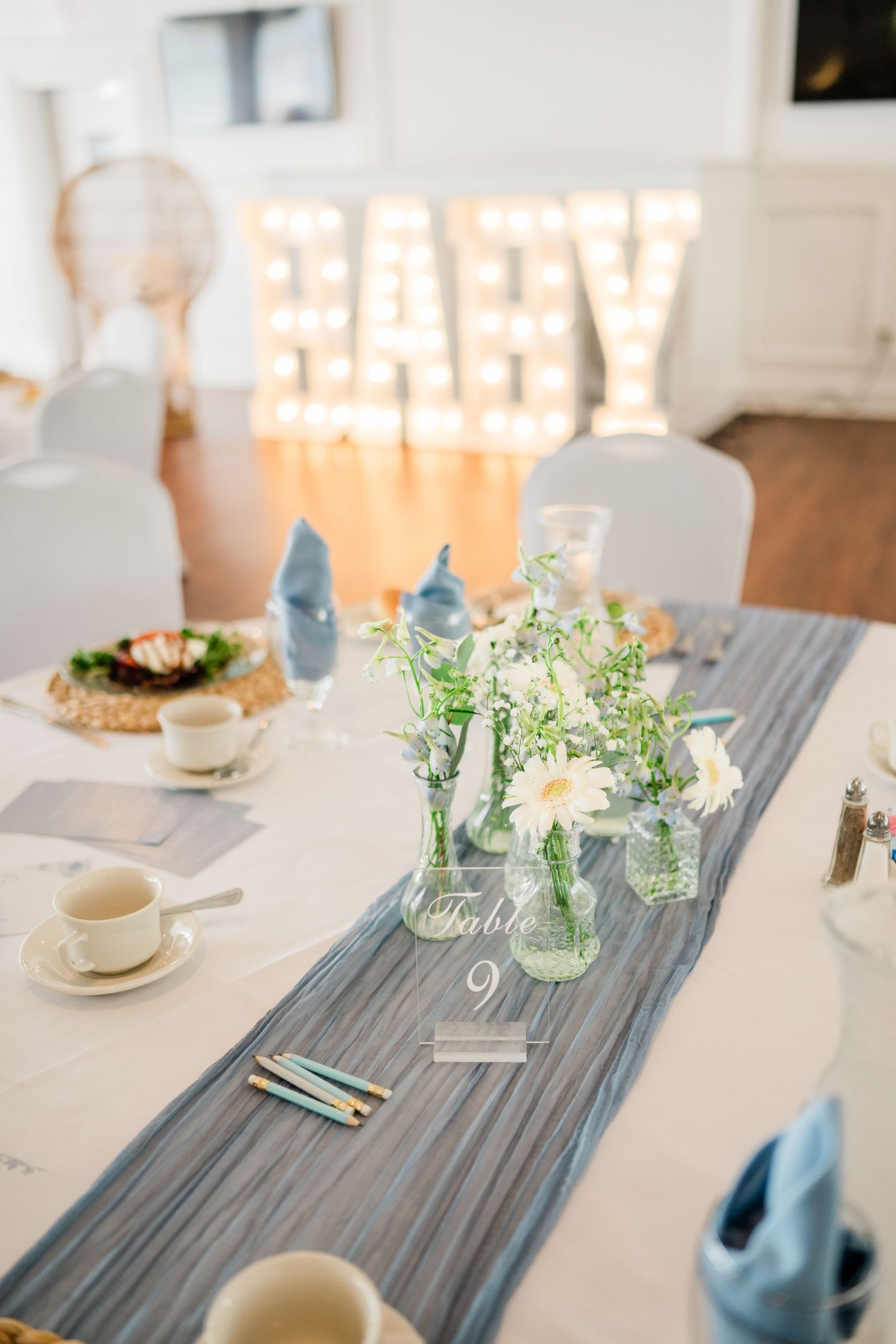 Elegant table setting with gray runner and lit BABY marquee sign in background.