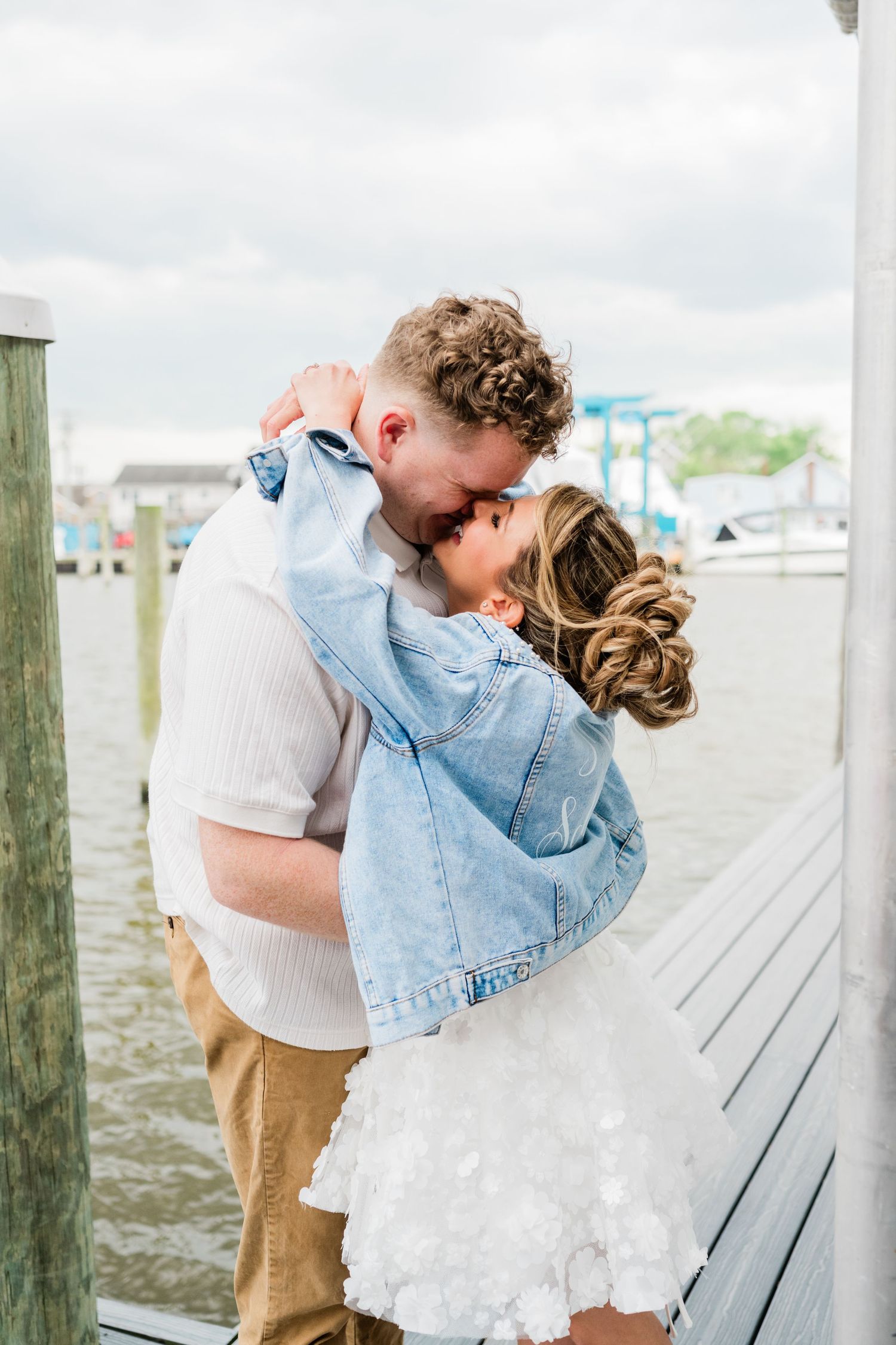 A romantic moment captured on a wooden dock by the water with a denim jacket detail.