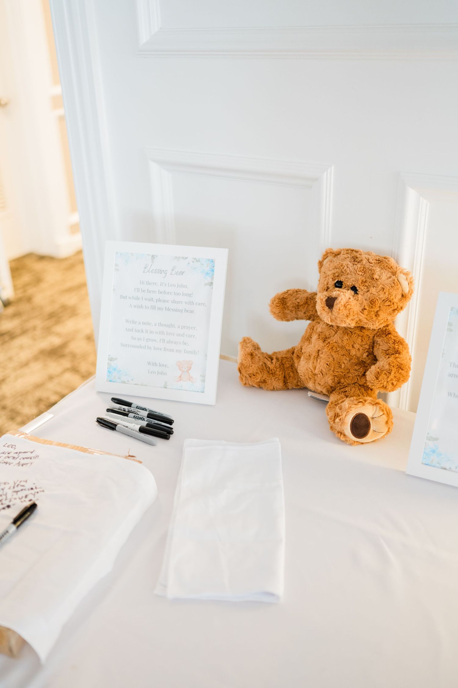 Guest book table with teddy bear and writing supplies for baby shower.