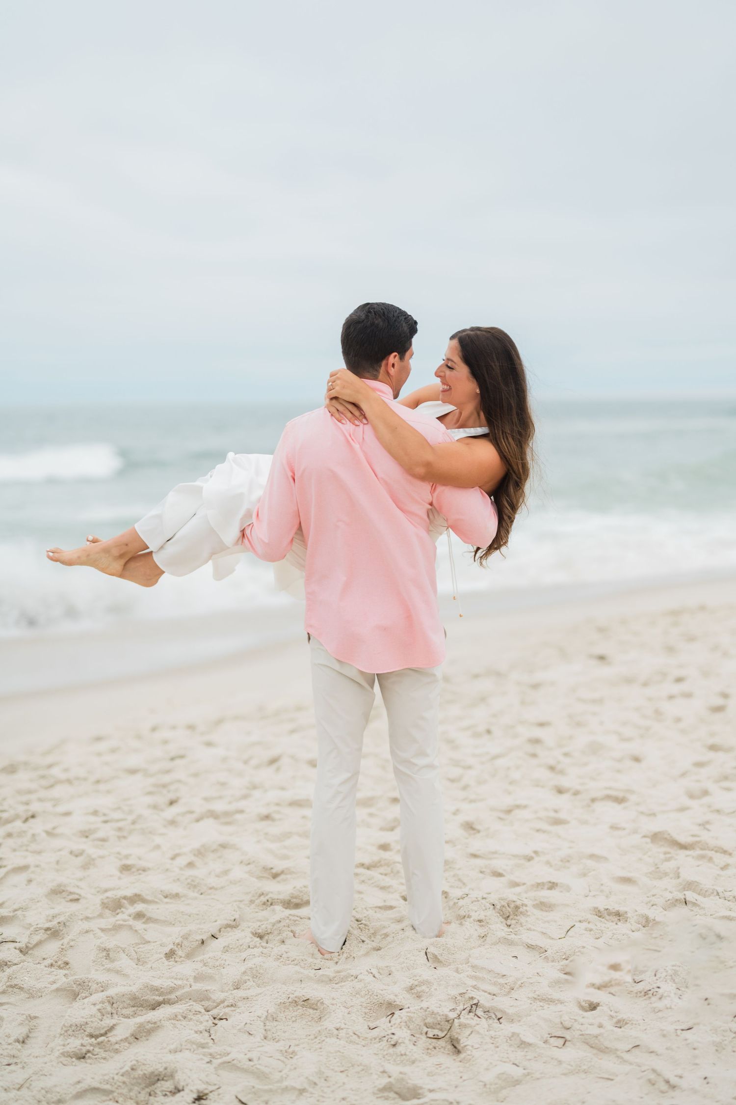 Playful couple spinning and dancing together on a sandy beach by the ocean.