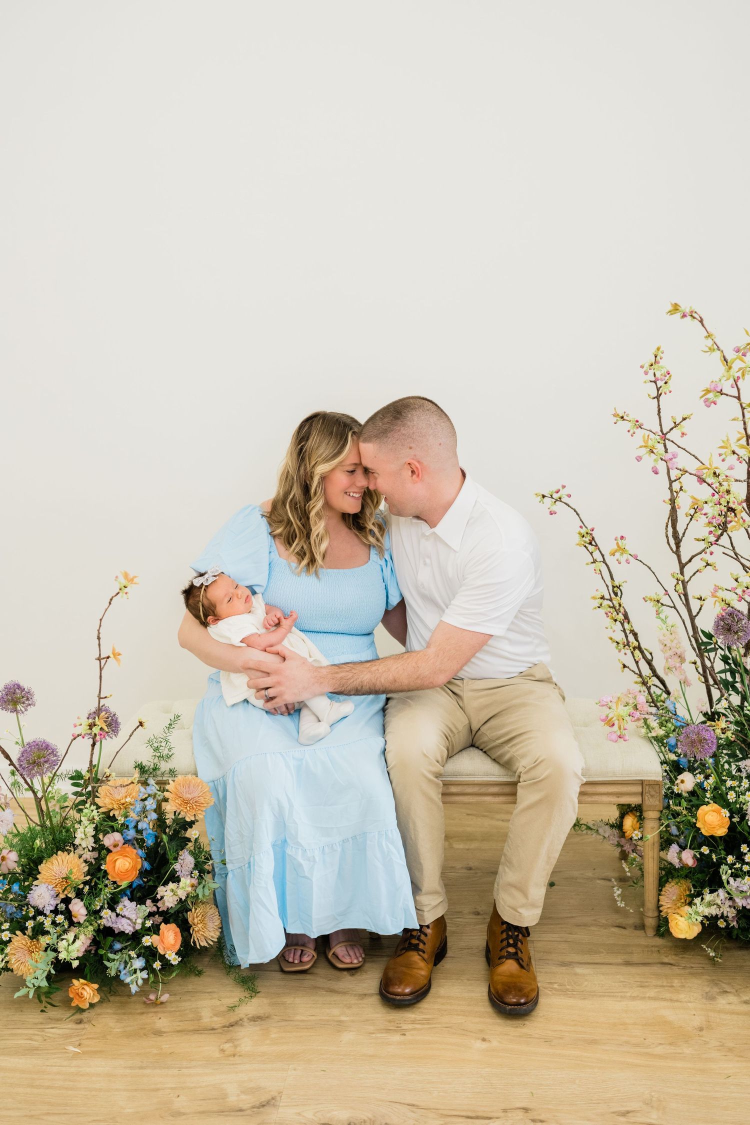 Romantic portrait session with floral arrangements and soft blue dress on wooden bench.