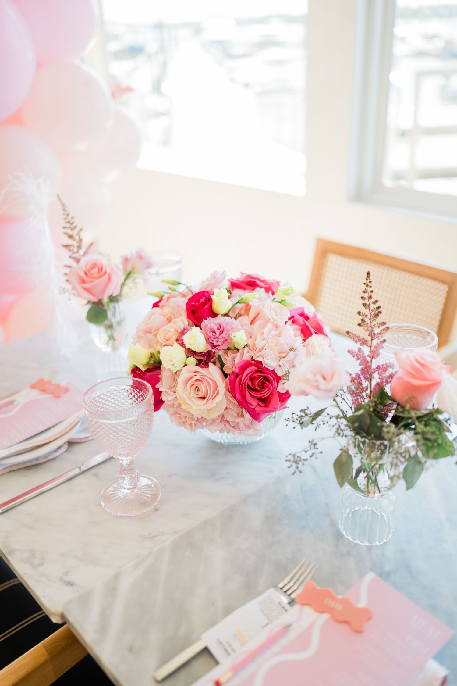 Pink and red floral centerpieces with roses arranged on white tablecloths for an elegant event.