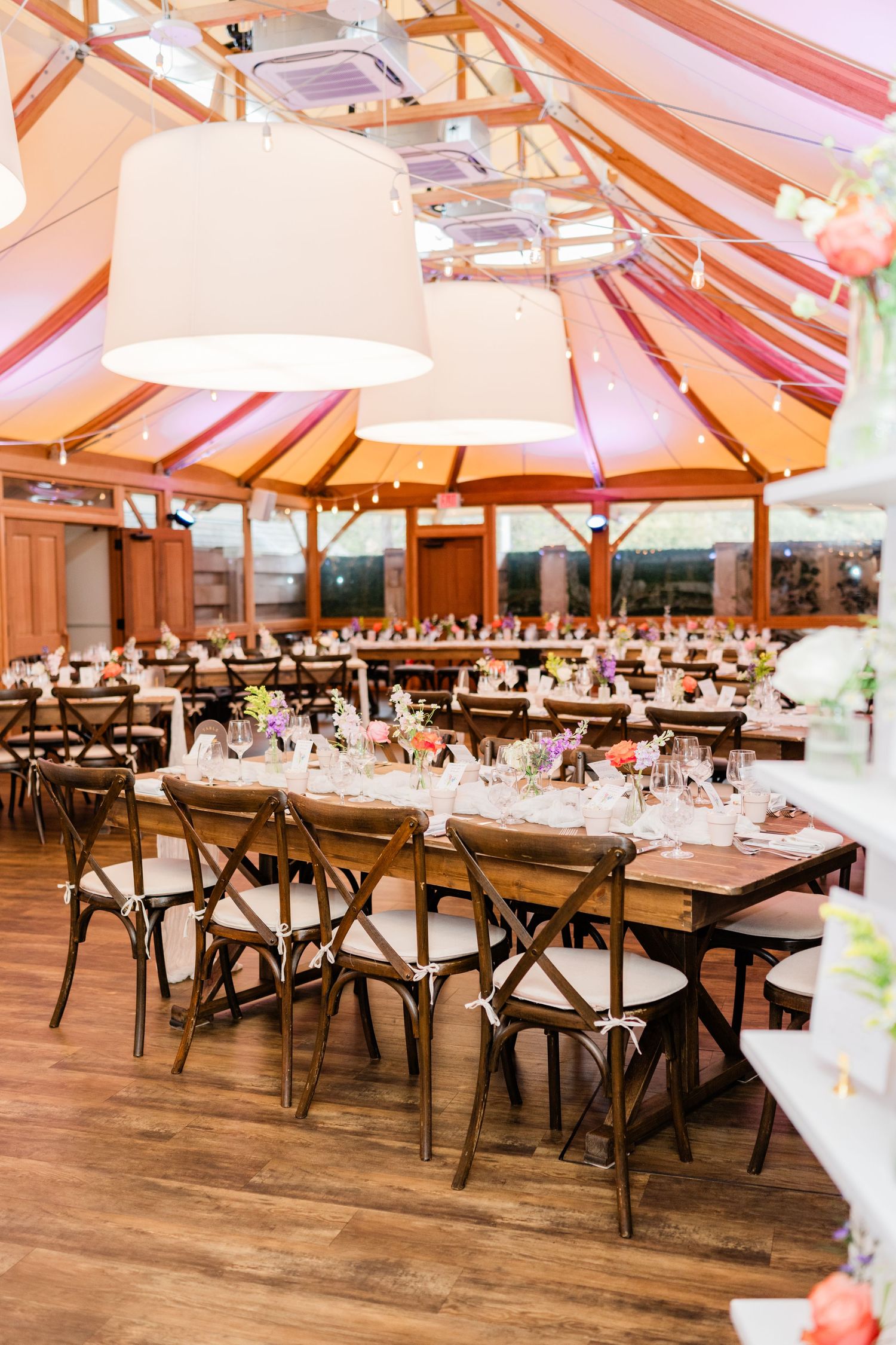Large wedding reception hall with wooden cross-back chairs and long banquet tables.