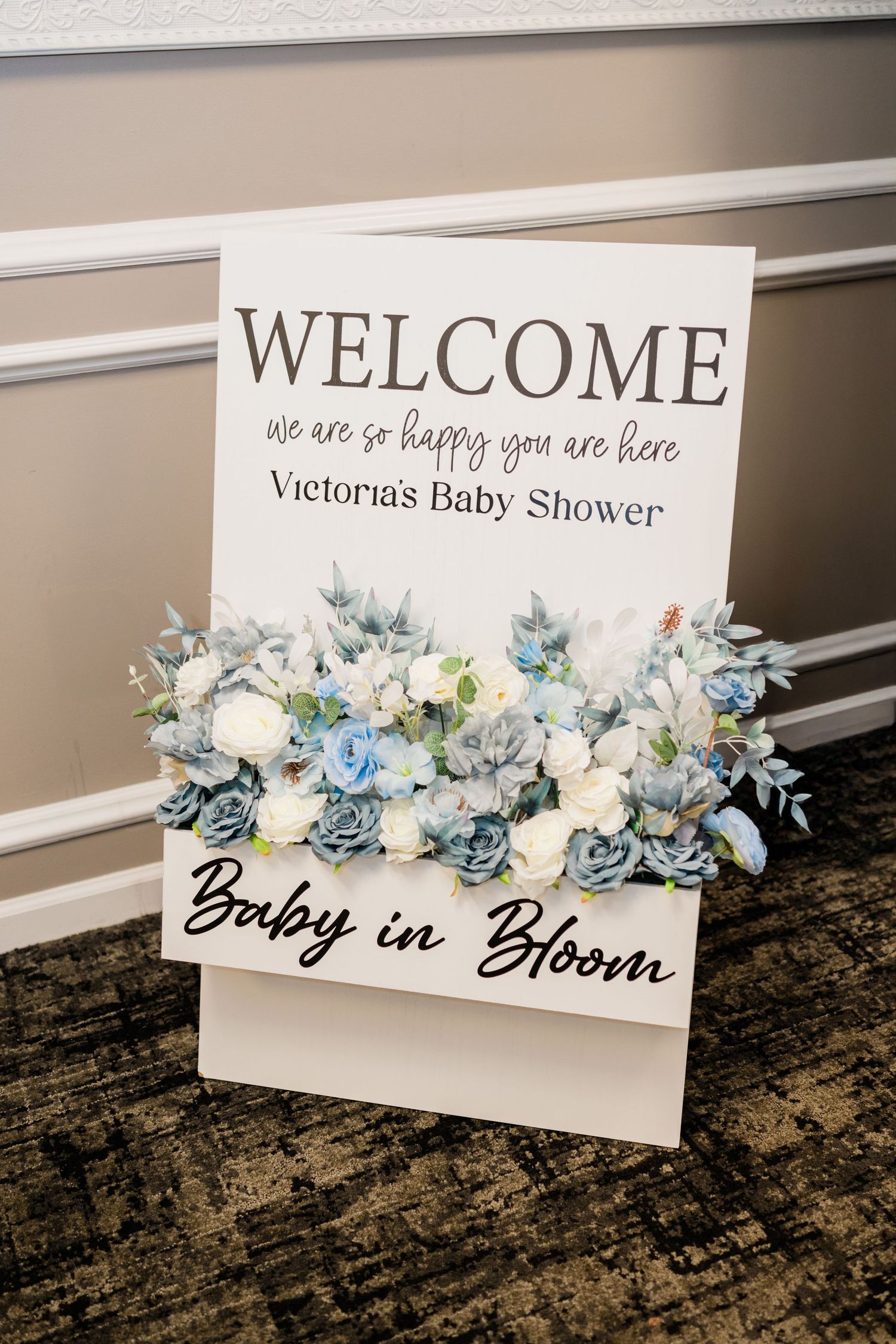 Welcome sign decorated with blue and white flowers for a baby shower event.