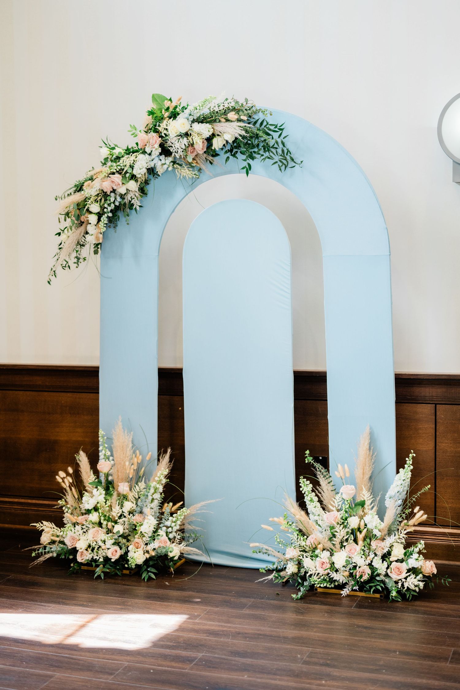 Light blue arched backdrop decorated with white and peach floral arrangements.
