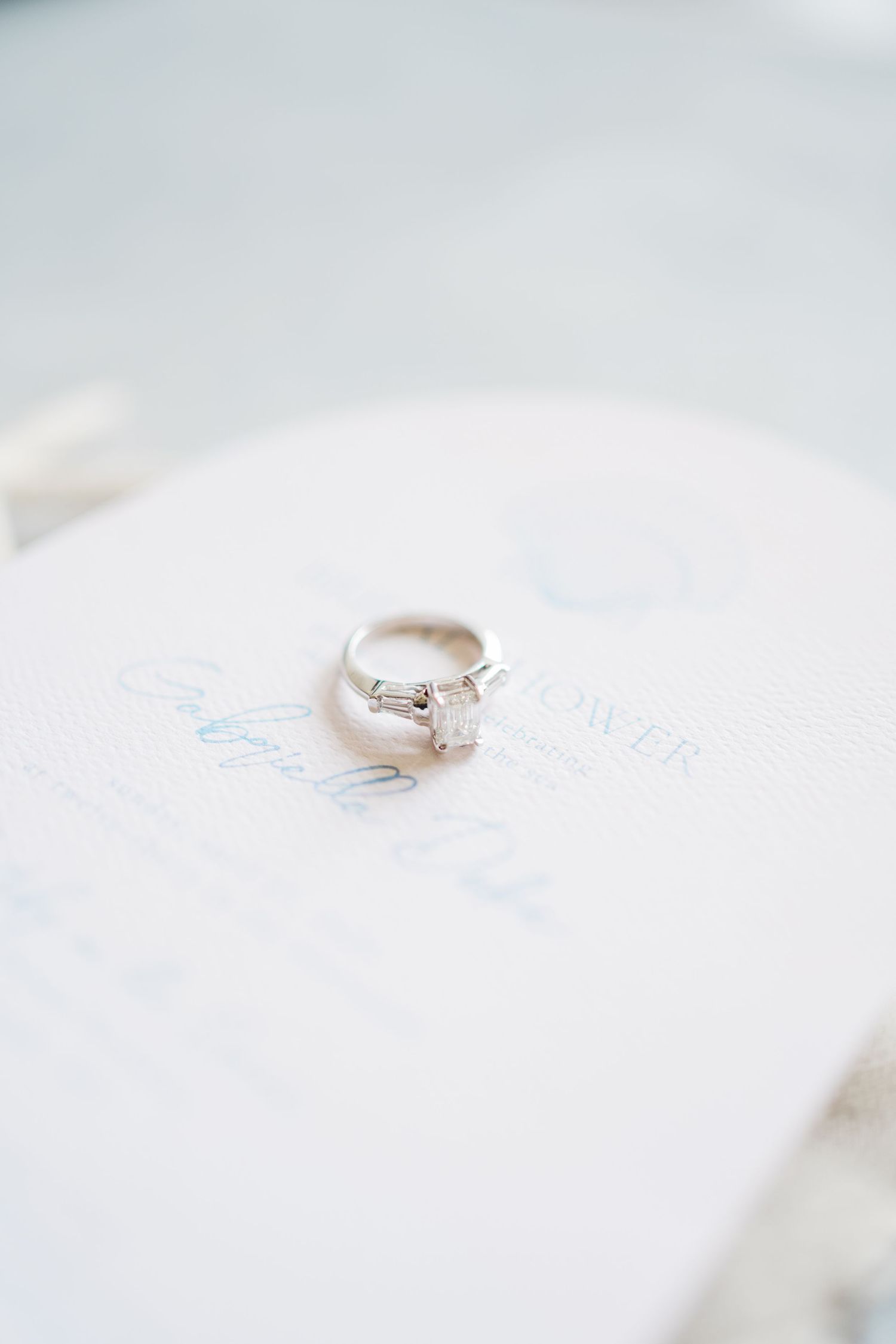 Diamond engagement ring photographed on white textured paper with soft natural lighting.