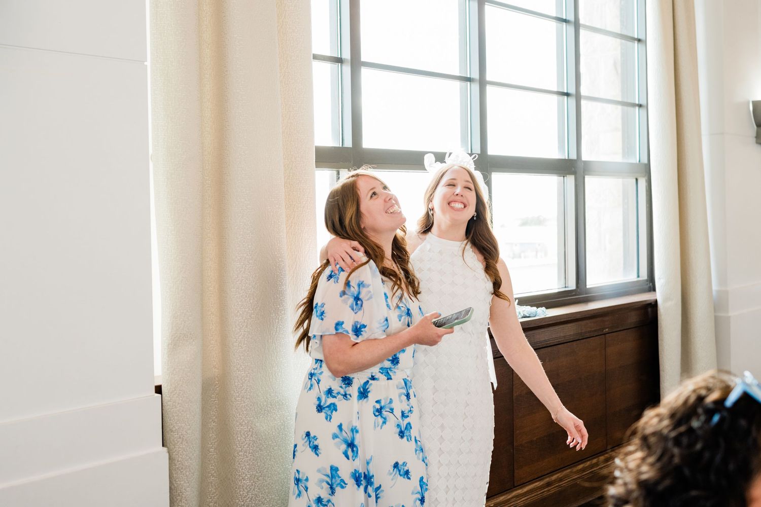 A blue floral dress twirls in natural window light creating an ethereal bridal shower scene.