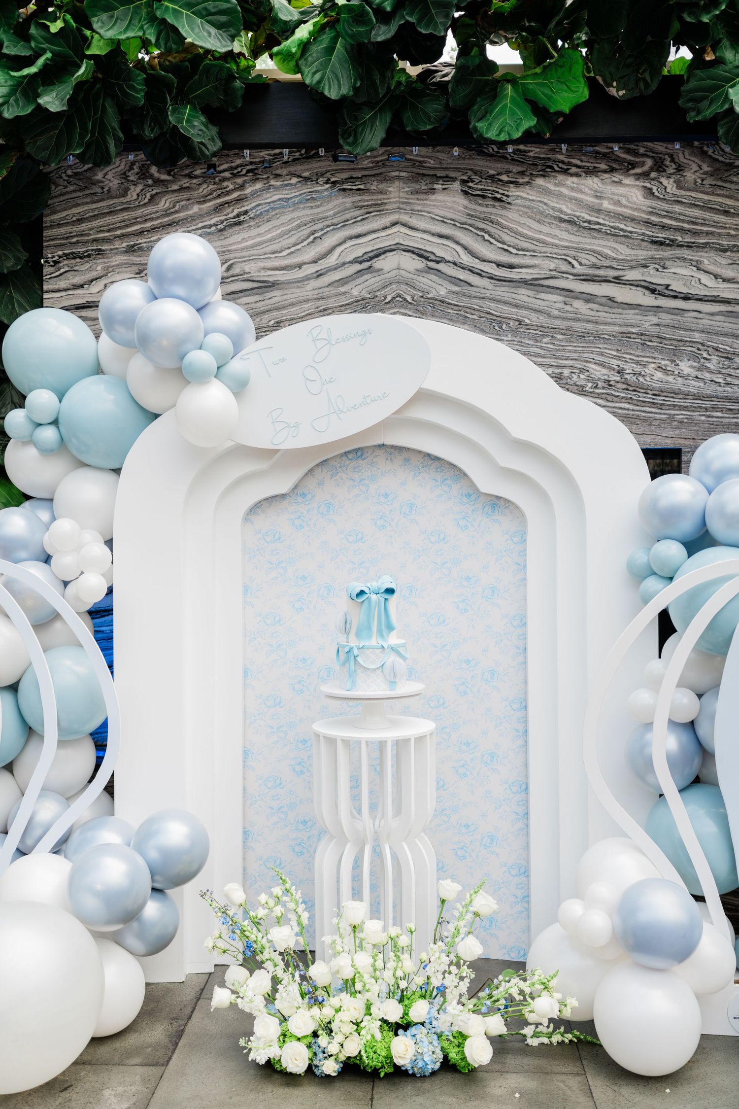 White and blue balloon arch with floral decorations and number 1 centerpiece against marble backdrop.