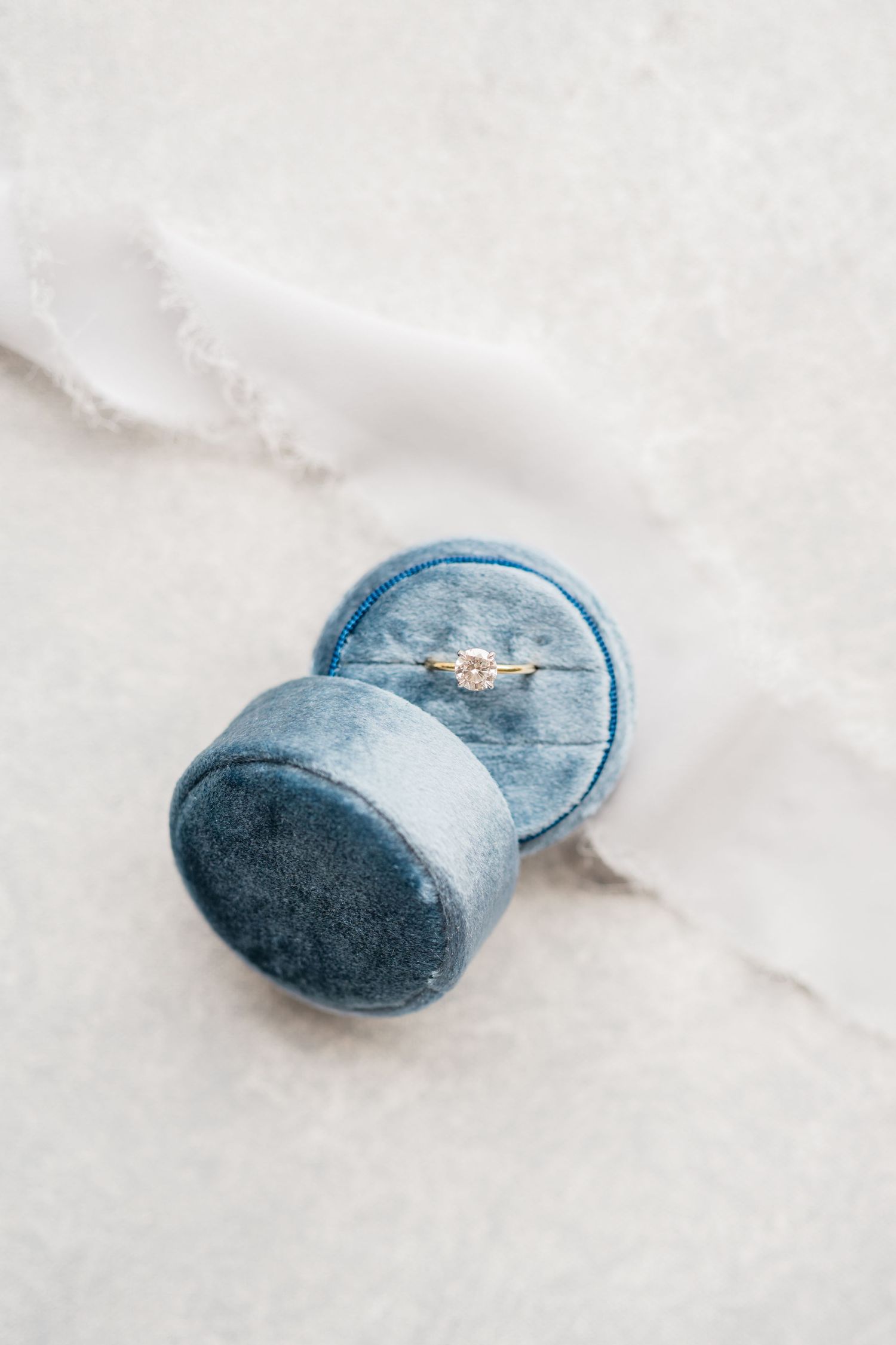Close-up series of a blue velvet ring box on white marble surface.