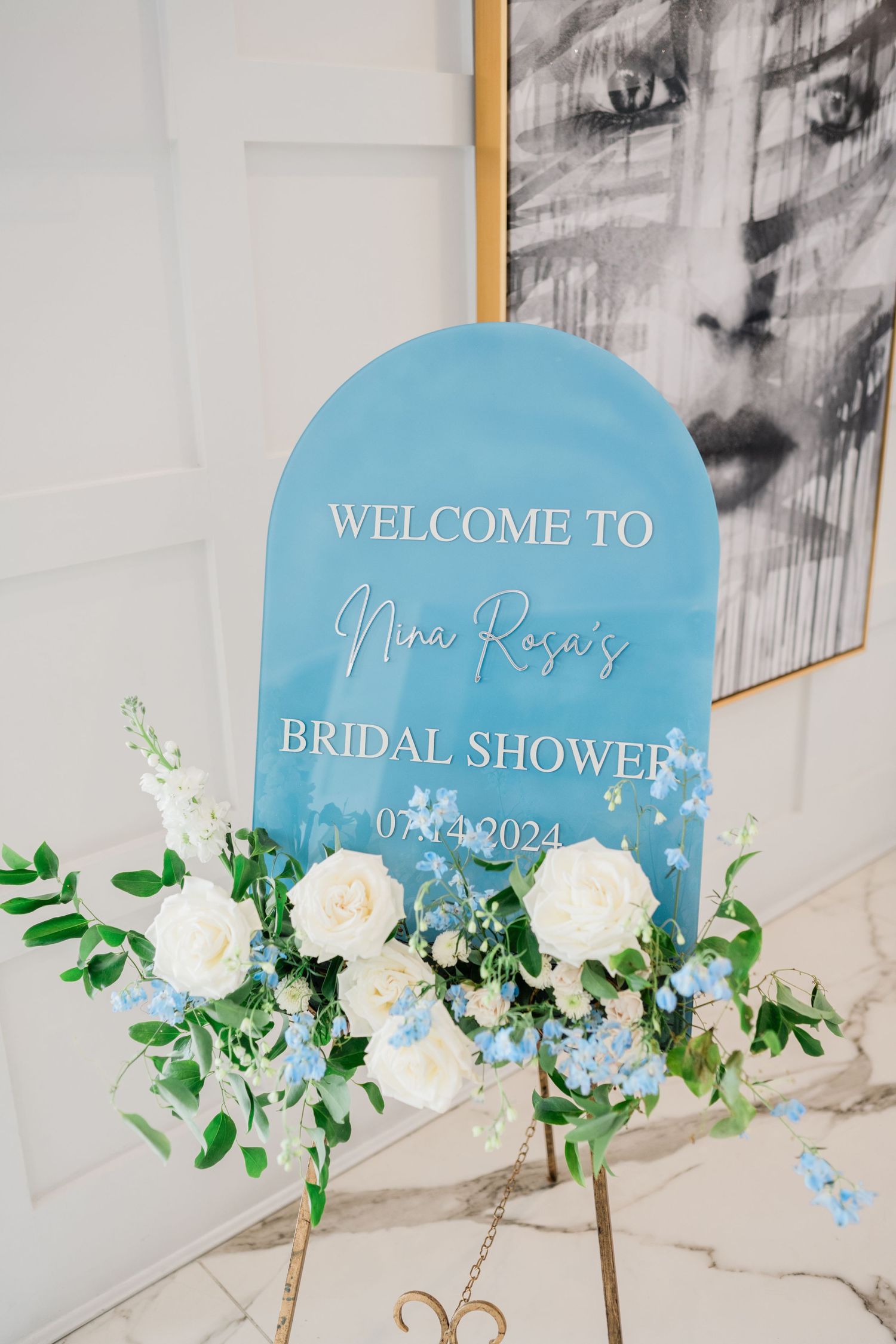 Blue welcome signs decorated with white roses and greenery for a bridal shower.