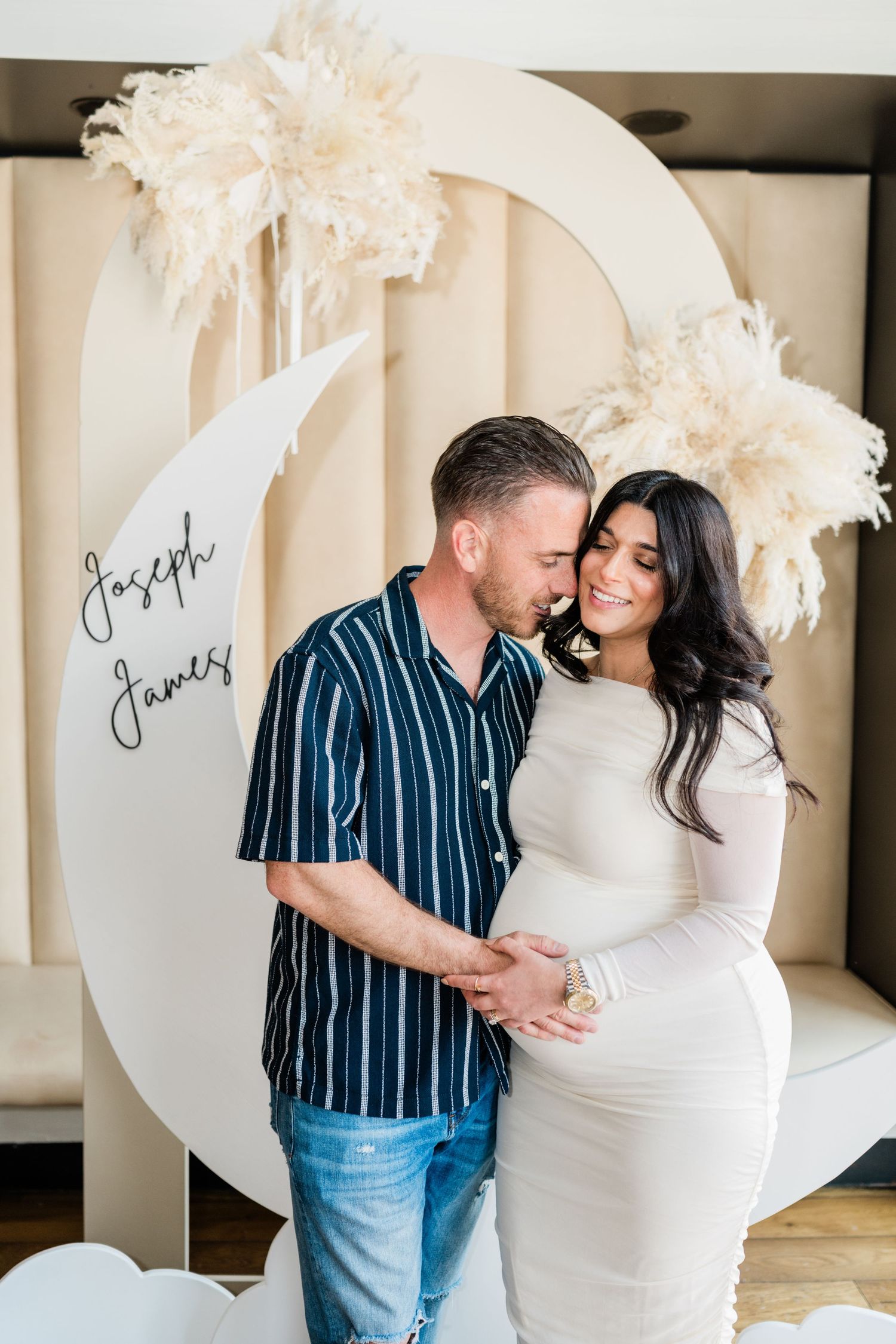 Maternity photo featuring a decorative moon backdrop with pampas grass details.