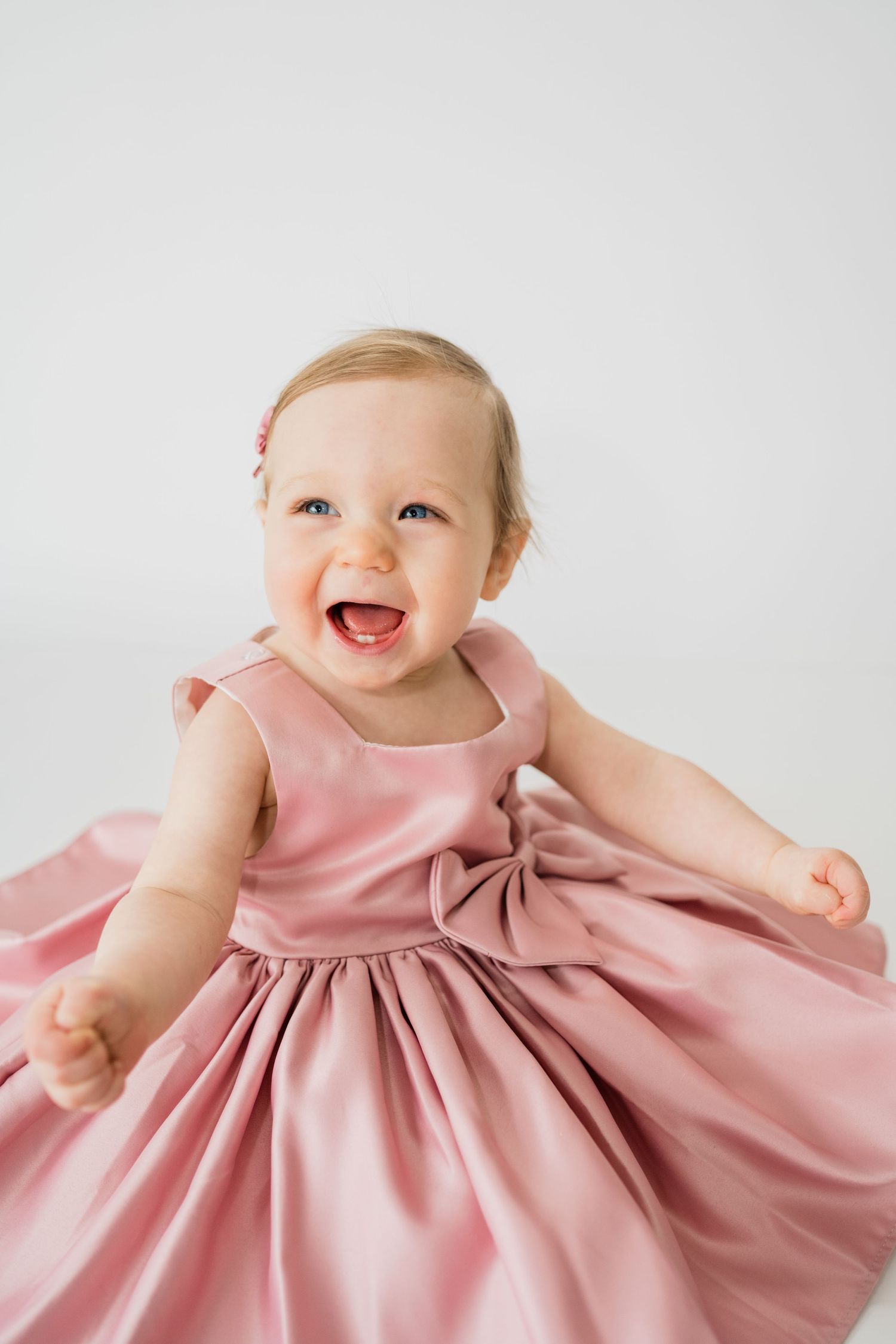 A pink satin dress with a bow detail twirls against a white background.