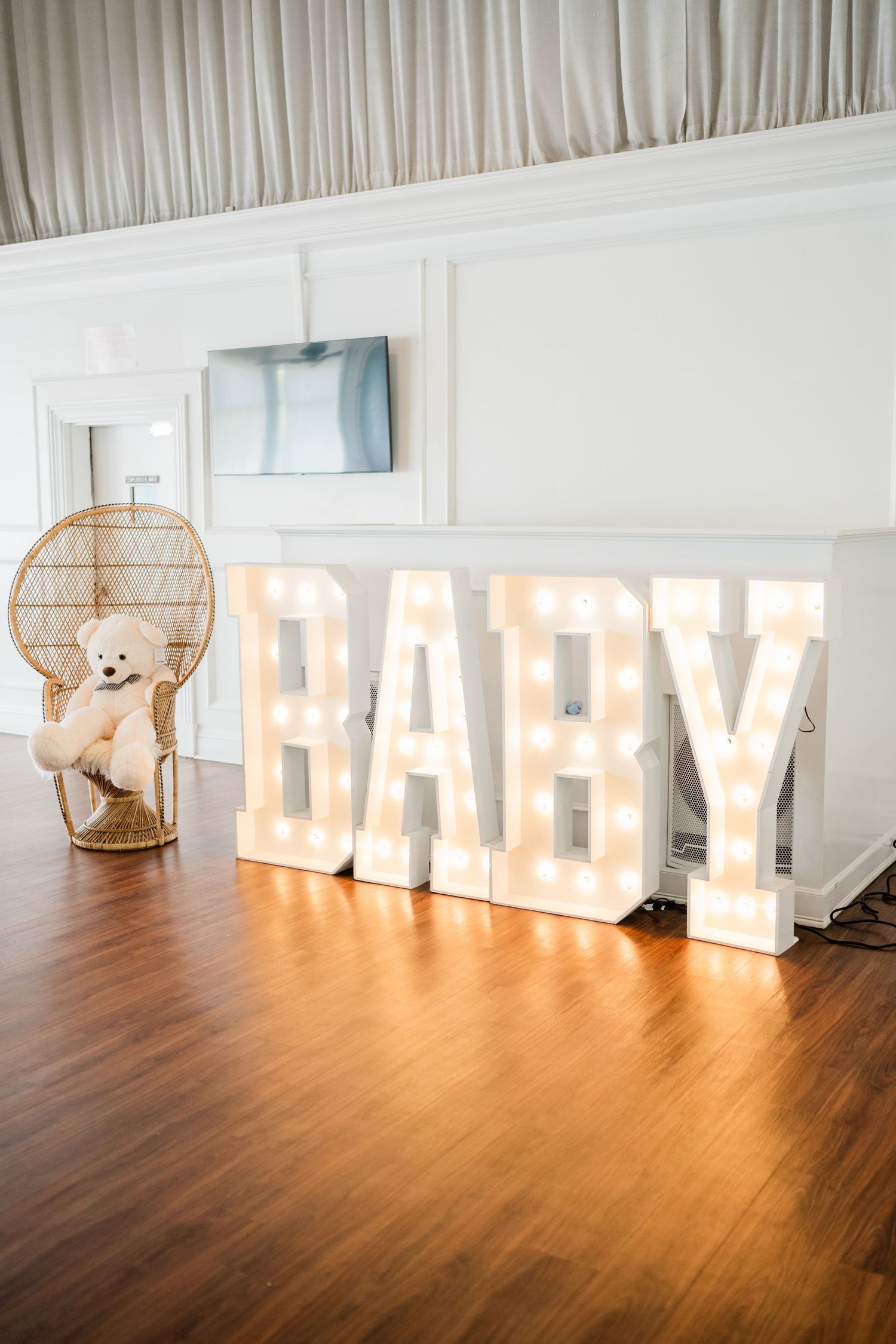 Illuminated BABY marquee letters with decorative teddy bear on wooden floor.