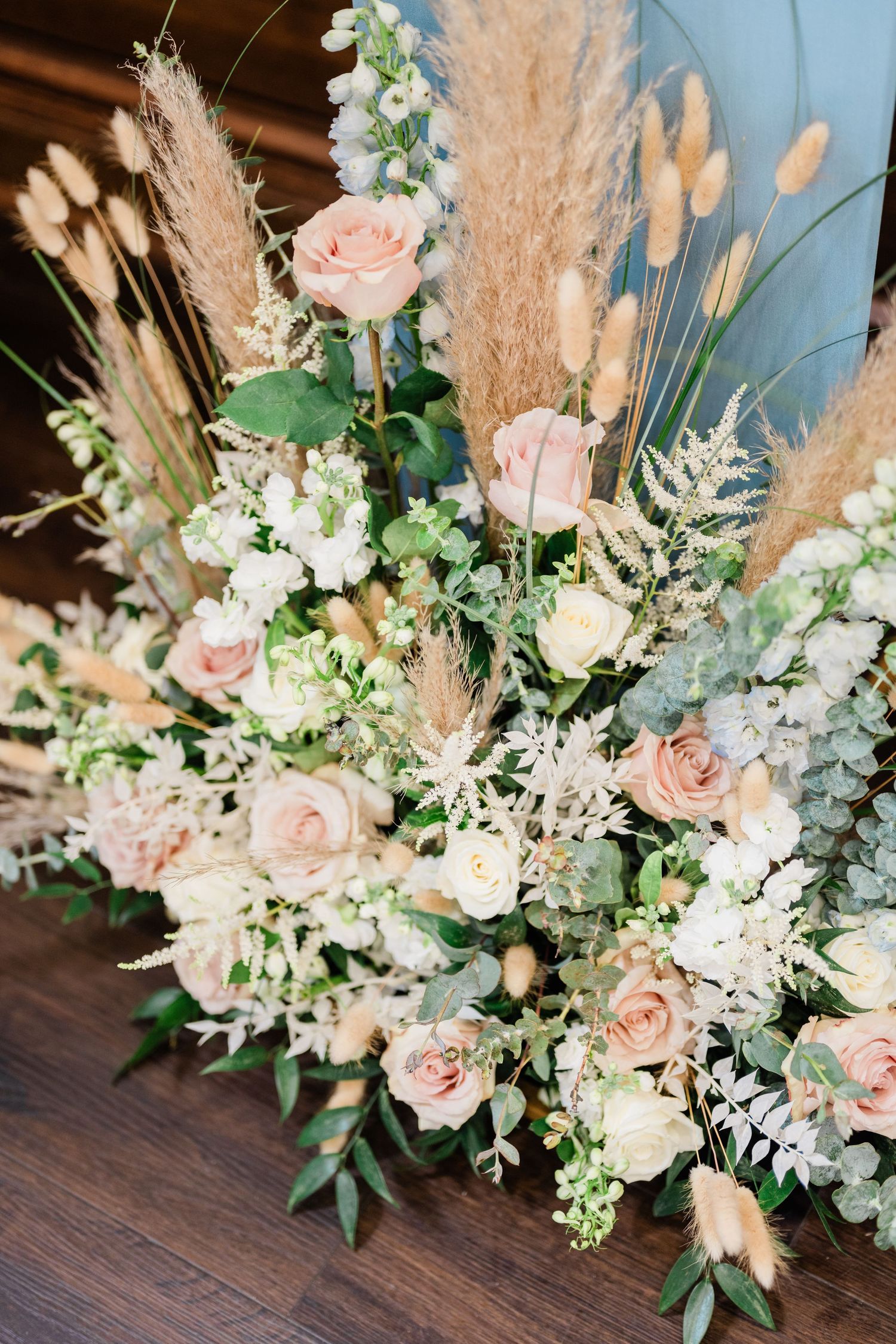 Lush floral arrangement featuring pampas grass, roses, and eucalyptus in soft pastel tones.