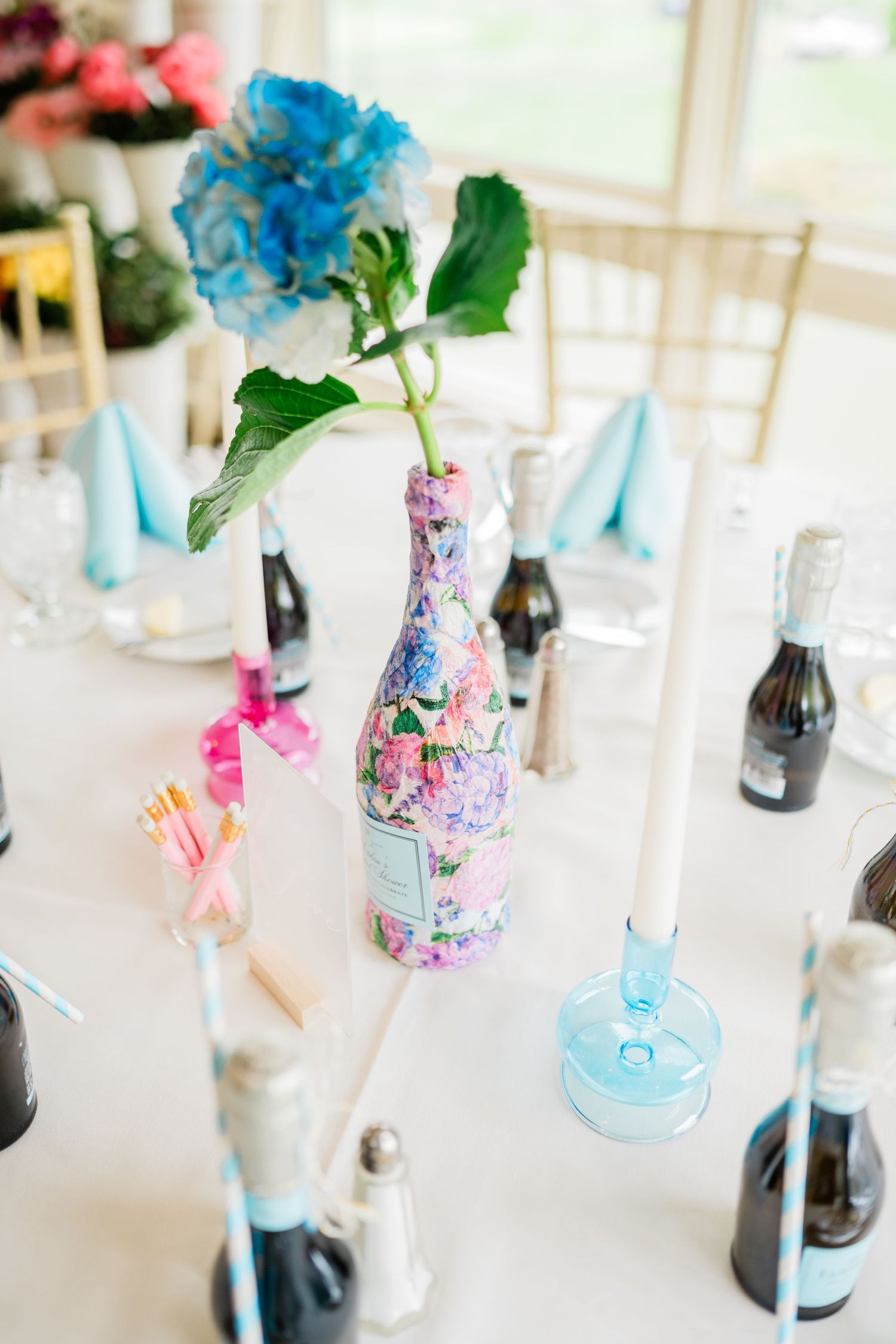 Wedding reception table decorated with blue flowers in painted vases and champagne bottles.