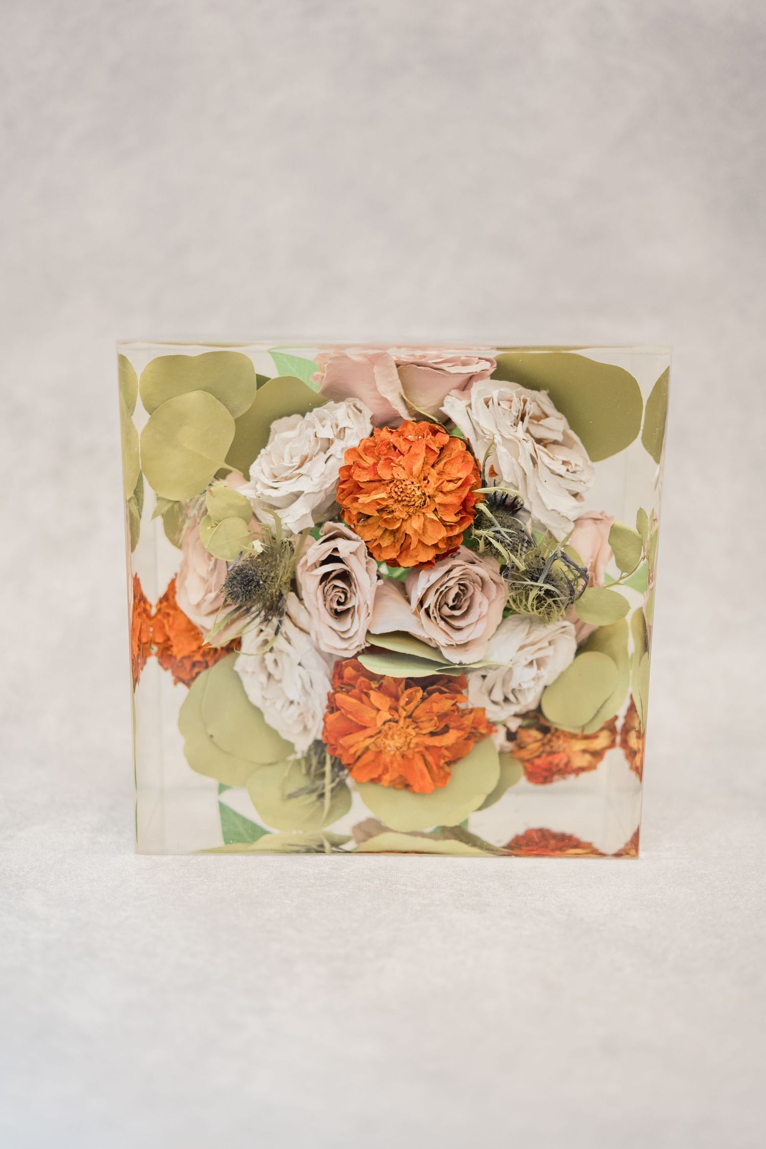 Floral arrangement in clear acrylic featuring peach roses and orange carnations.