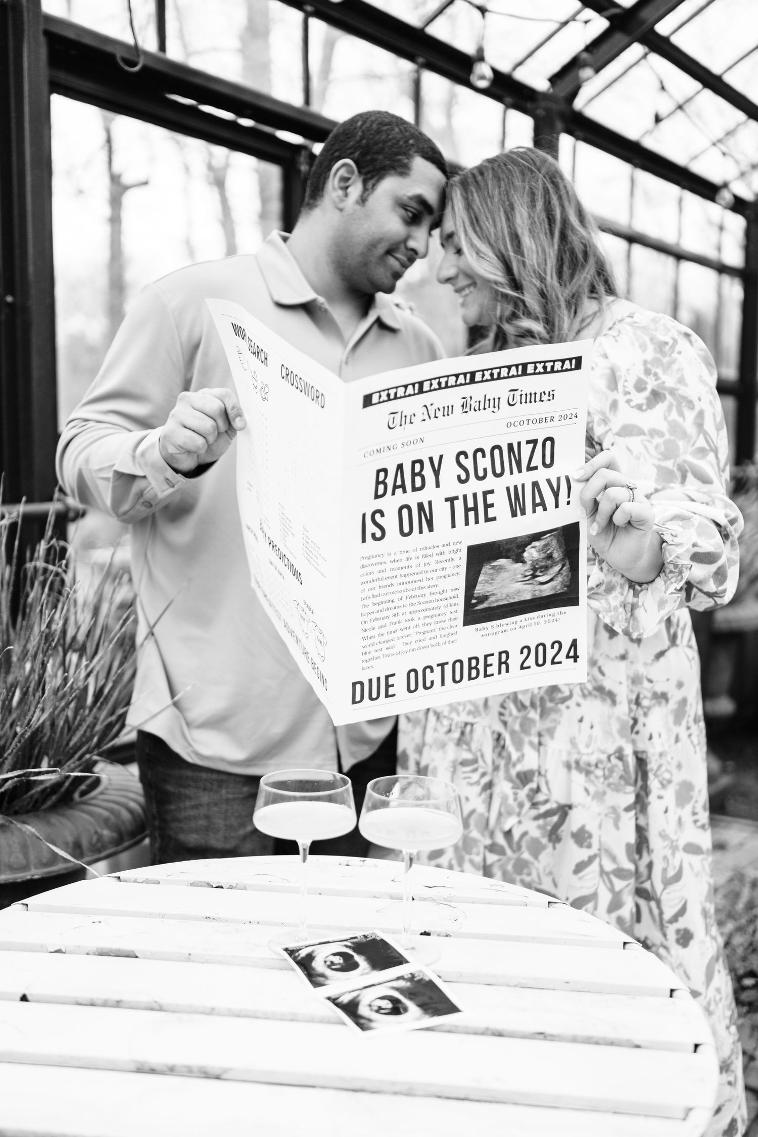 Couple holds newspaper pregnancy announcement in greenhouse setting.