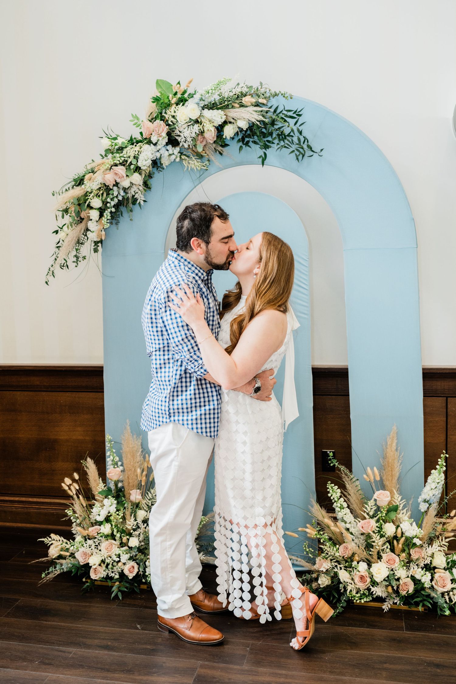 A romantic moment captured in front of a light blue archway decorated with white flowers.