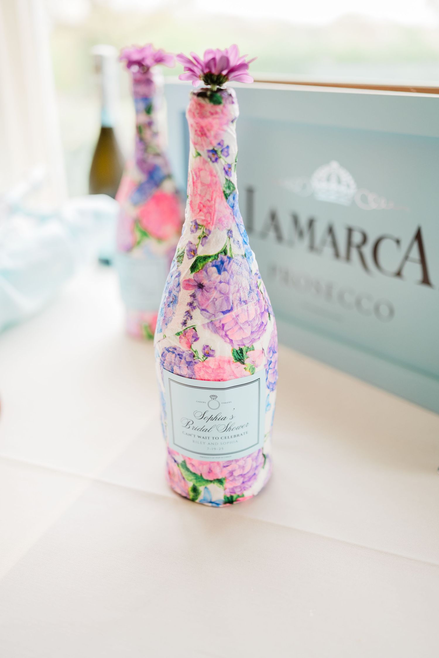 Decorative pink floral champagne bottle with delicate label displayed on white surface.
