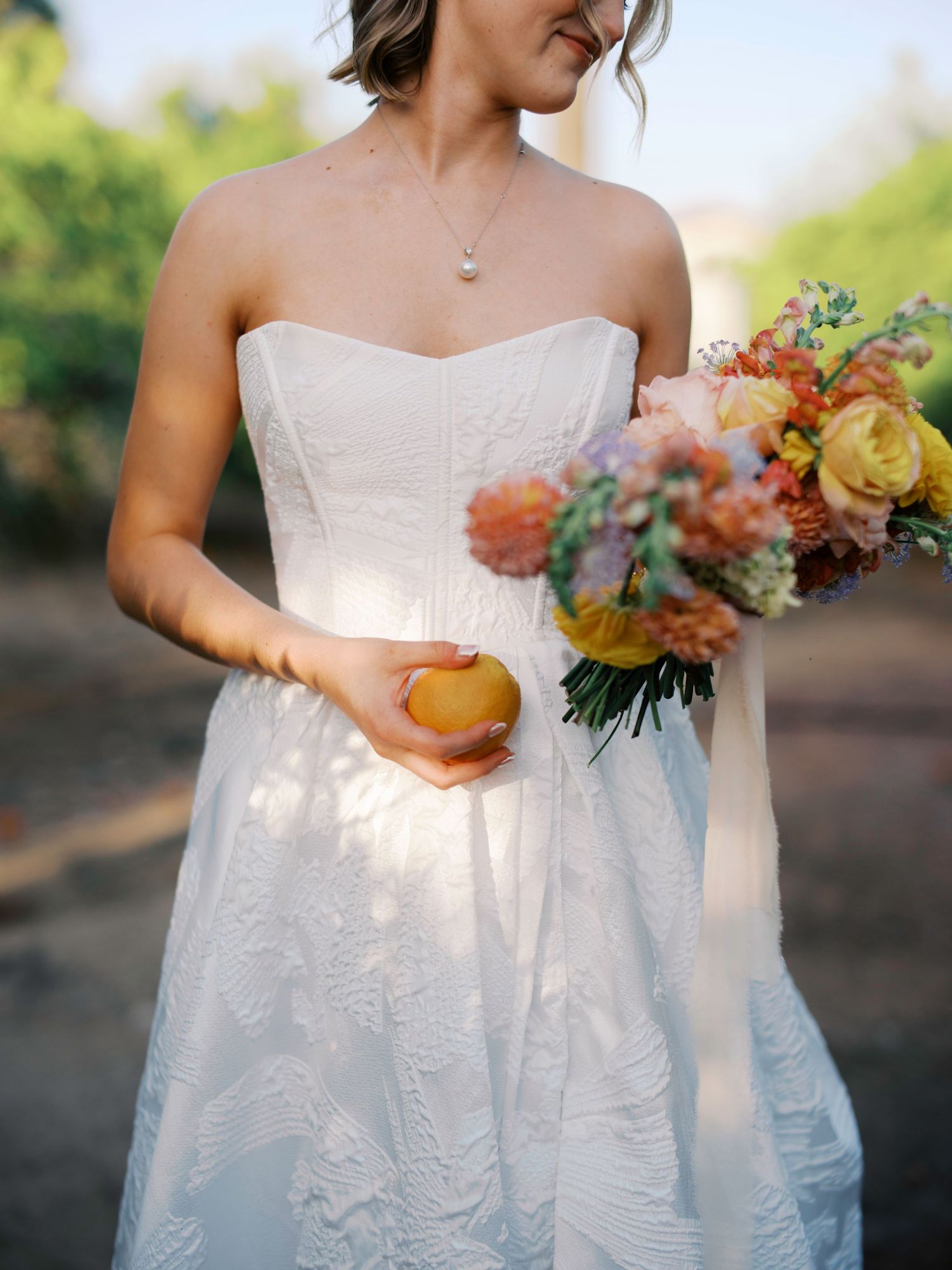 A close-up of a bridal bouquet made with autumn colored flowers and foliage held against a white dress in soft light.