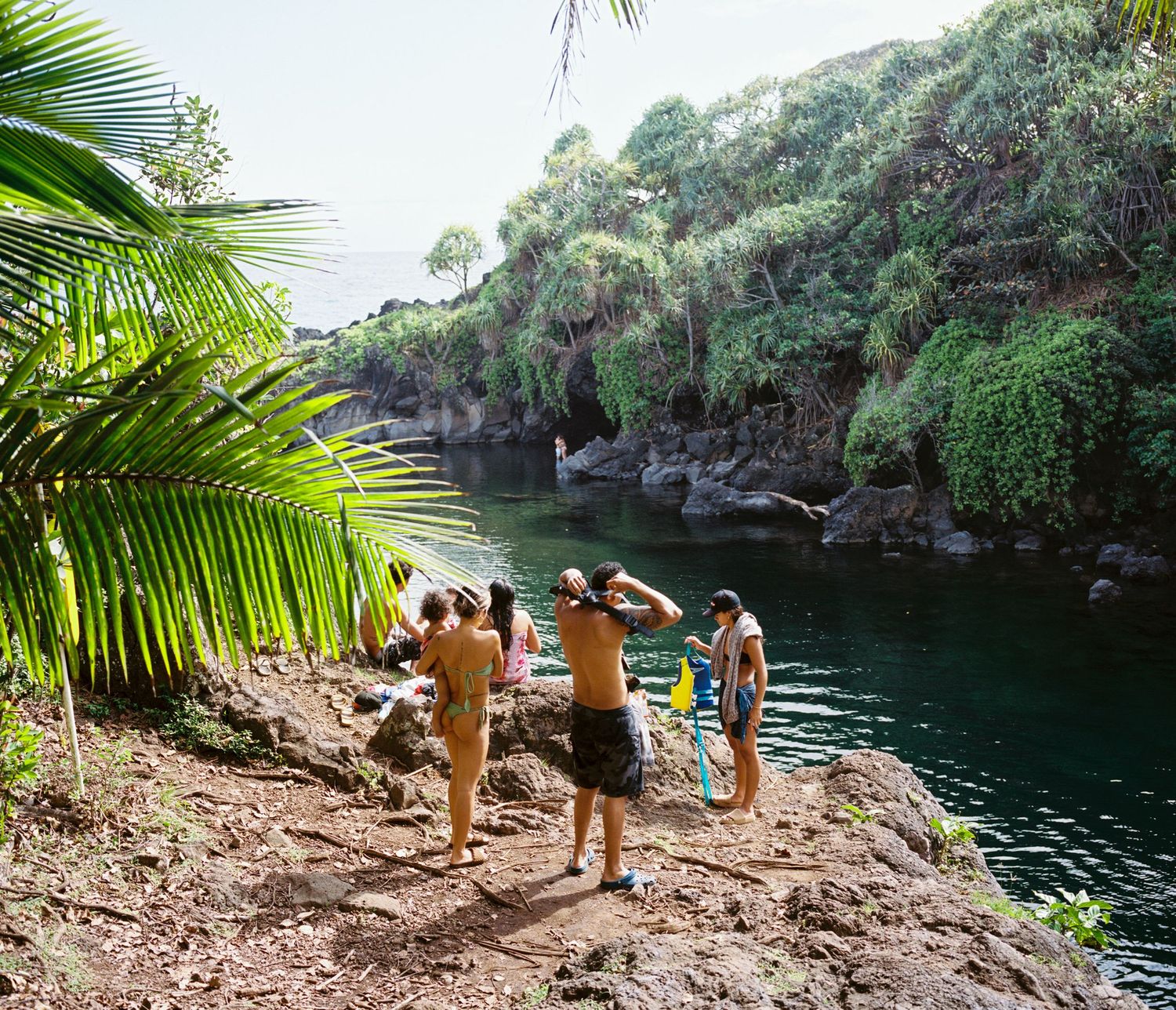 Group of hikers enjoying view of tropical swimming hole surrounded by lush vegetation.