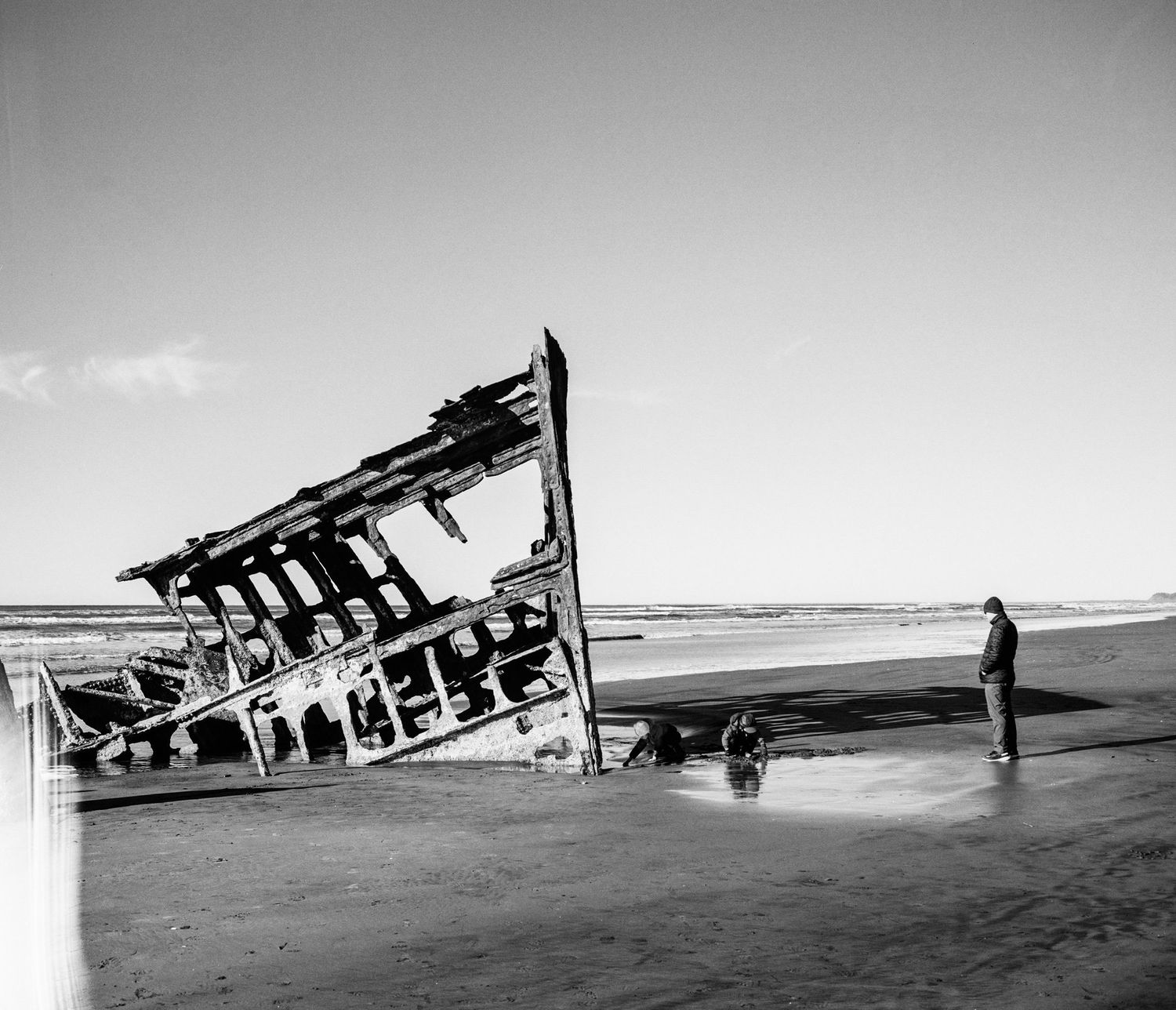 A shipwreck on a beach with a solitary figure standing nearby.
