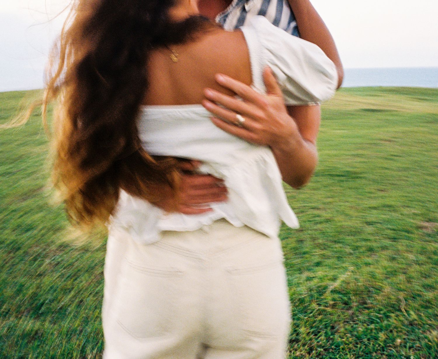 An intimate embrace captured in a field of green grass on a sunny day.