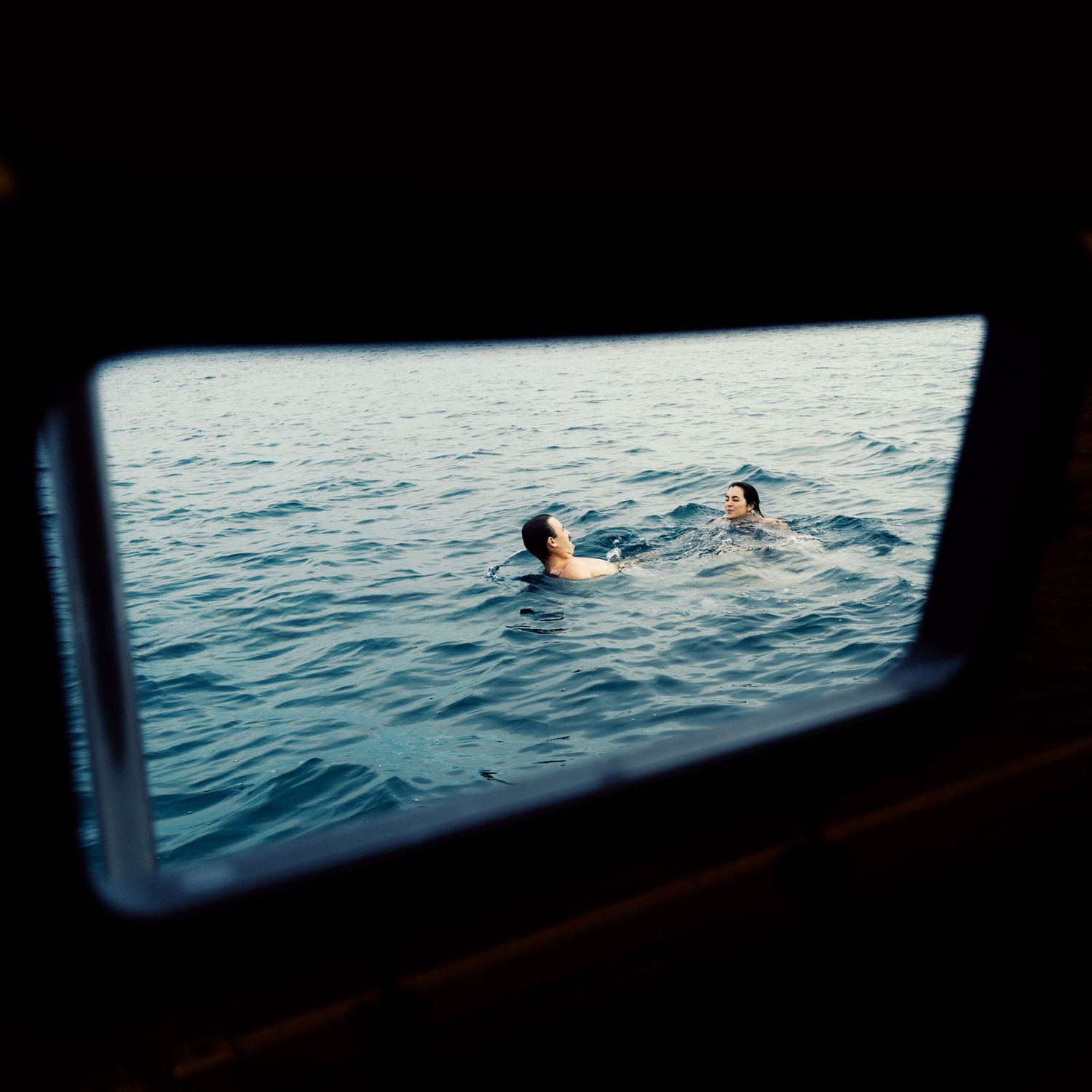 View through a window frame of people swimming in calm blue ocean waters.