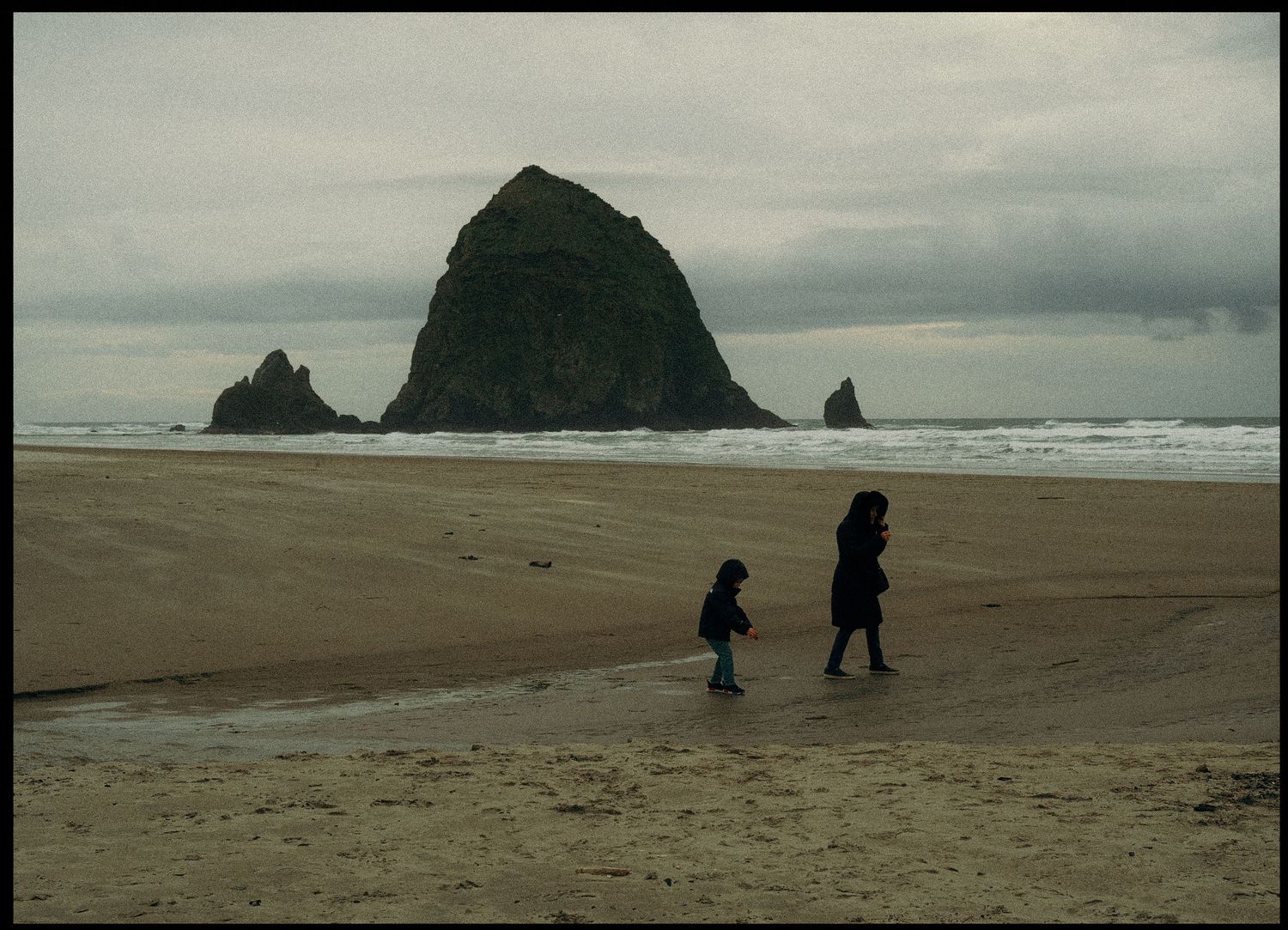 Two figures walking on beach with iconic Haystack Rock formation at Cannon Beach.