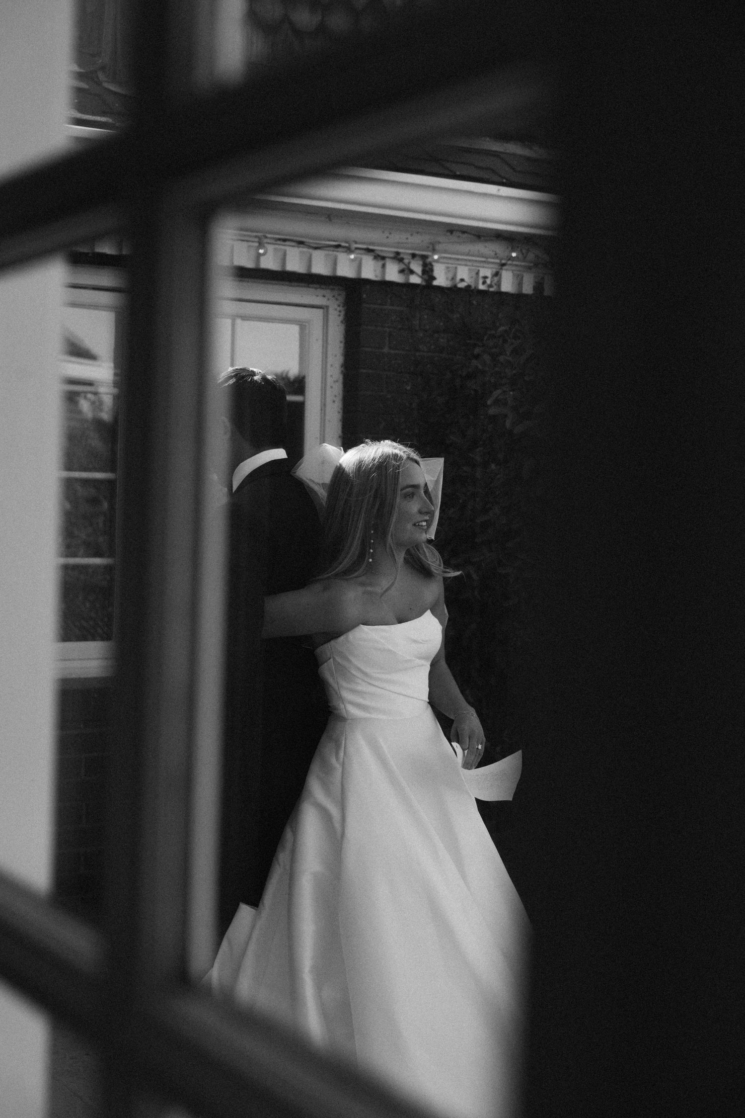 Black and white photograph of a bride in flowing white dress through window panes.