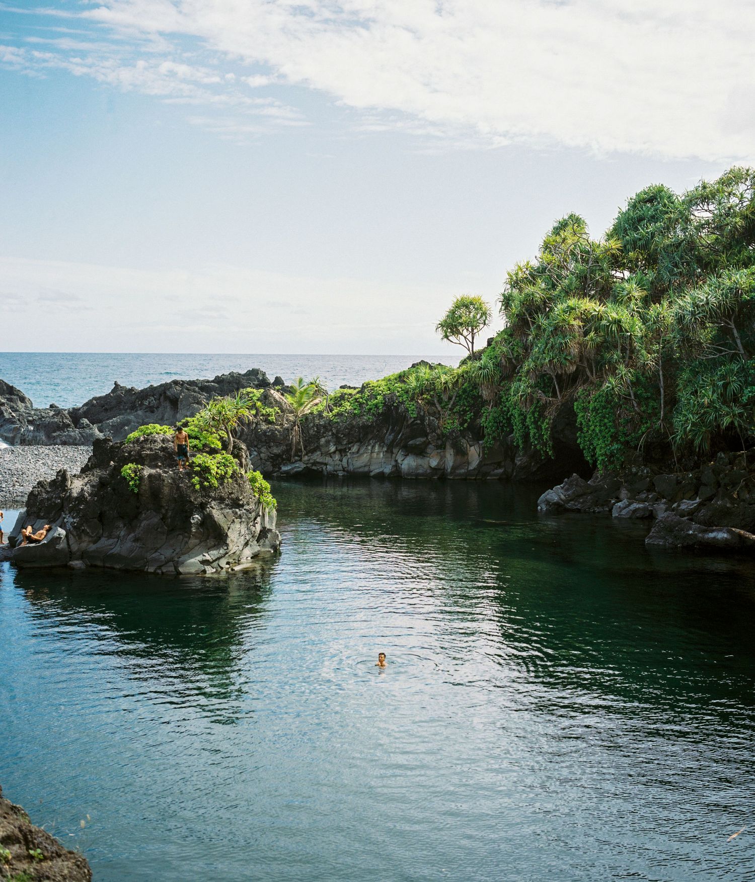 A secluded rocky cove with crystal clear turquoise water surrounded by lush vegetation and cliffs.
