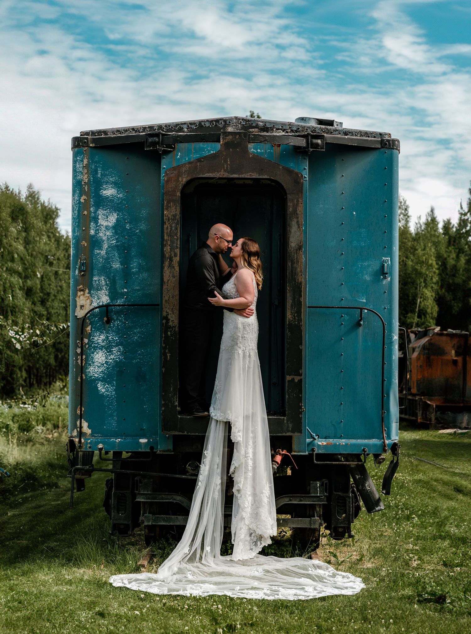 Bride and groom share a romantic kiss in the doorway of a vintage teal train car in wasilla alaska