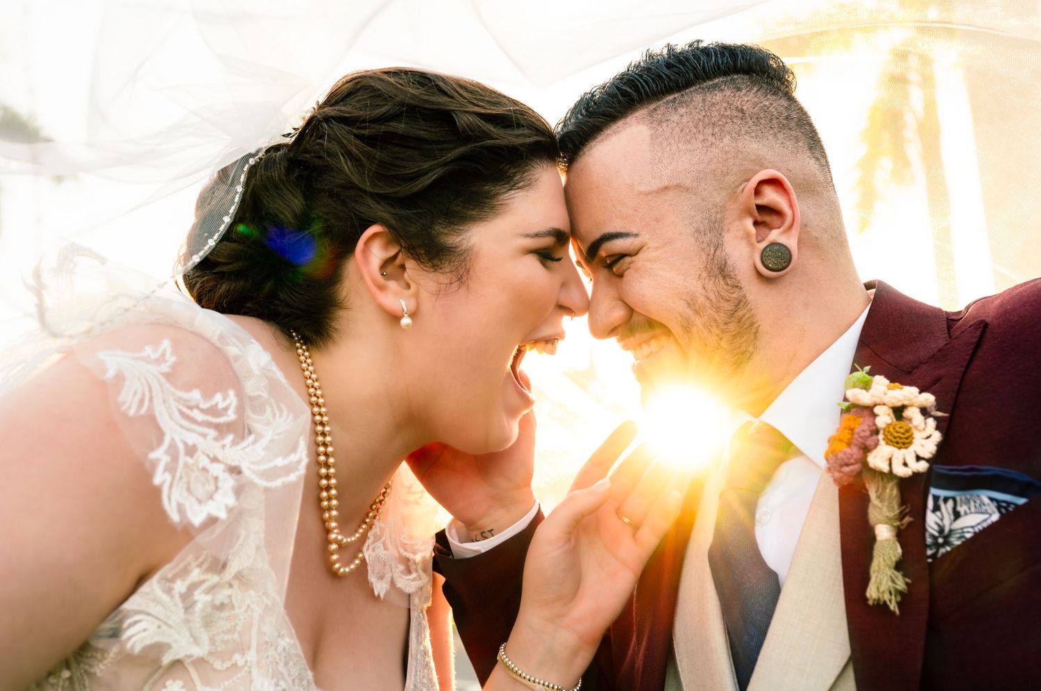 Joyful bride and groom touching foreheads and laughing together in golden sunlight on their wedding day.