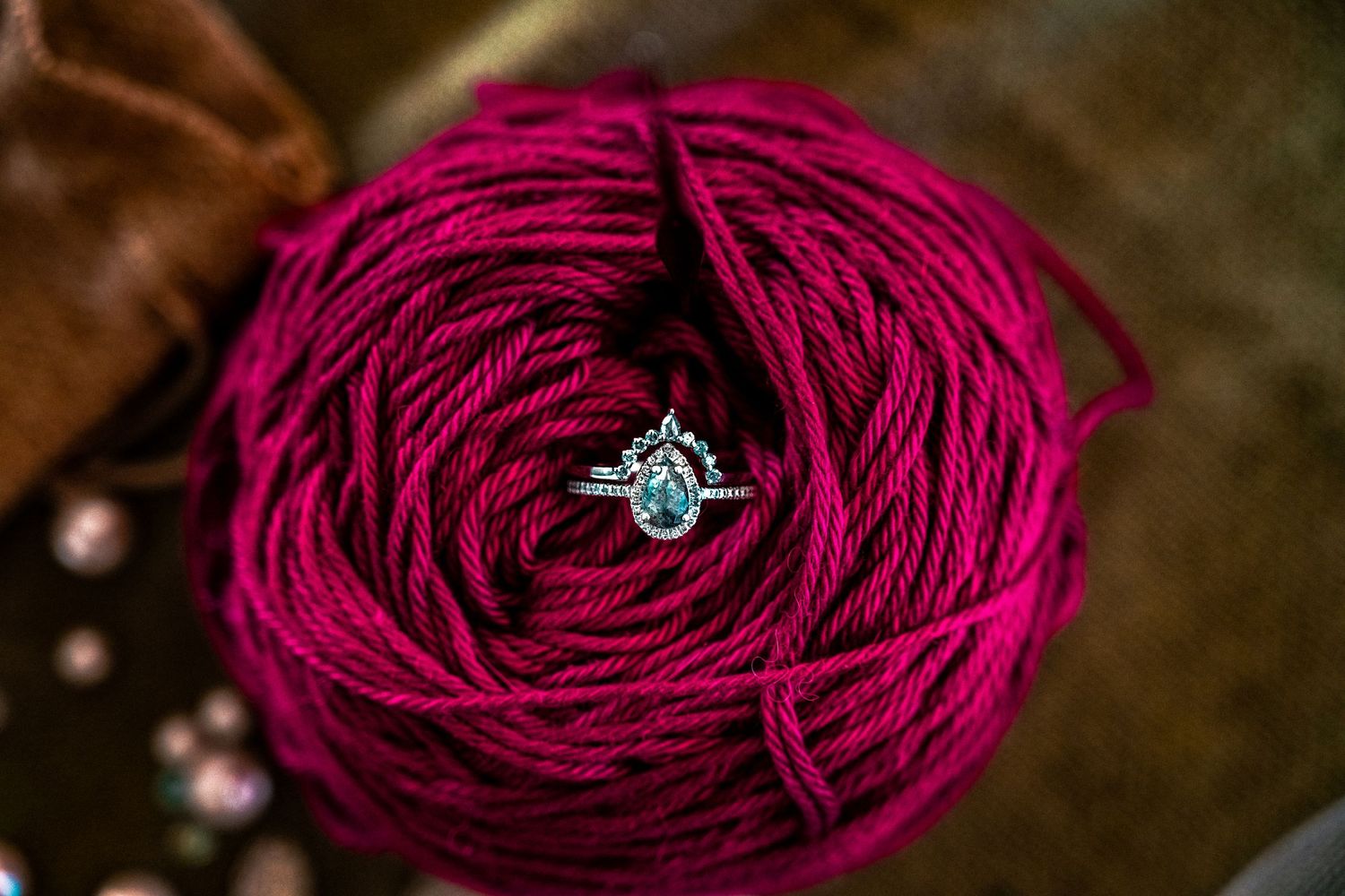 Silver diamond engagement ring resting on a vibrant magenta yarn ball, elegant jewelry photography.