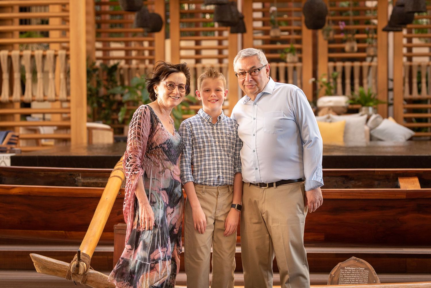Family of three smiling together in a beautiful tropical resort venue with wooden decor.