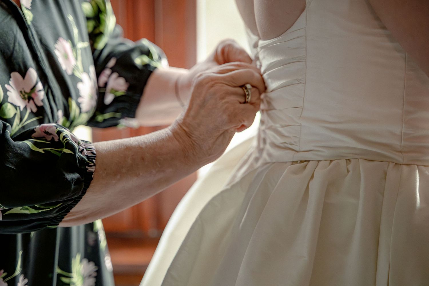 Mother helping bride button up the back of her white wedding dress.