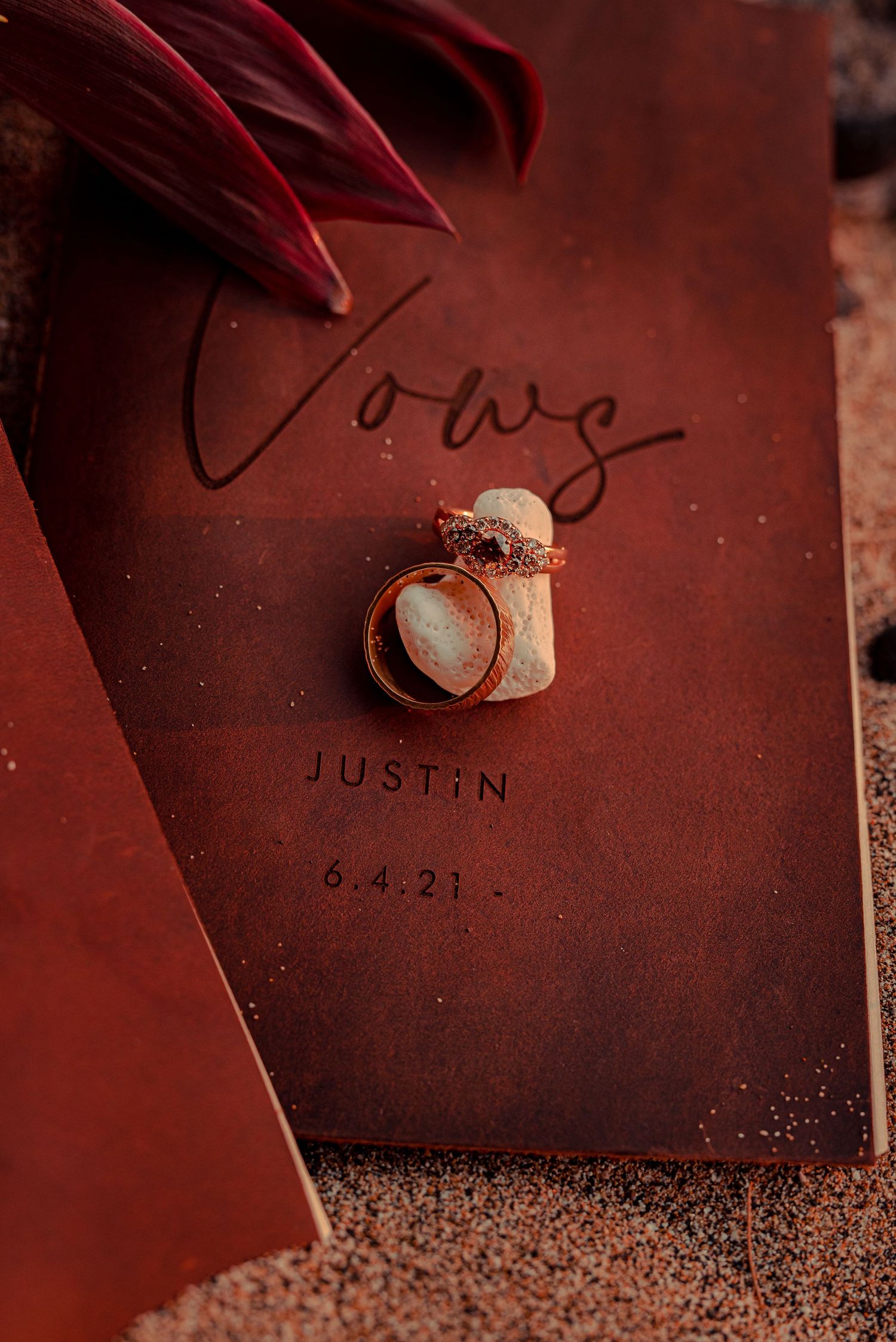 Wedding rings and vows card with 'Justin 6.4.21' text against a deep red background.