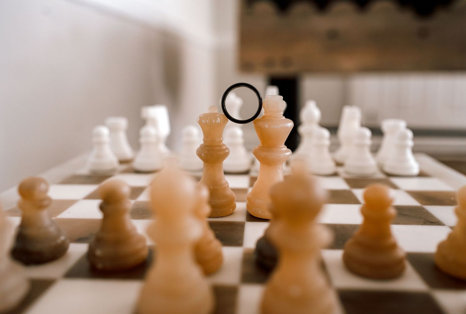 Detail shot of a groom's ring balanced between King and Queen chess pieces.