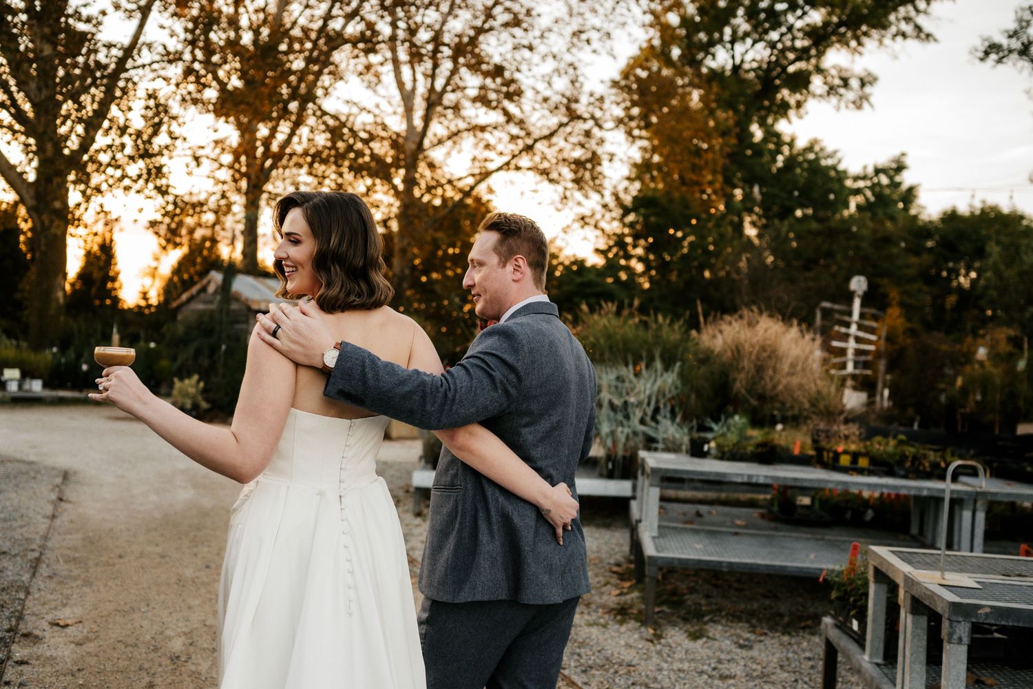 A couple in wedding attire dancing together at sunset in an outdoor garden setting.