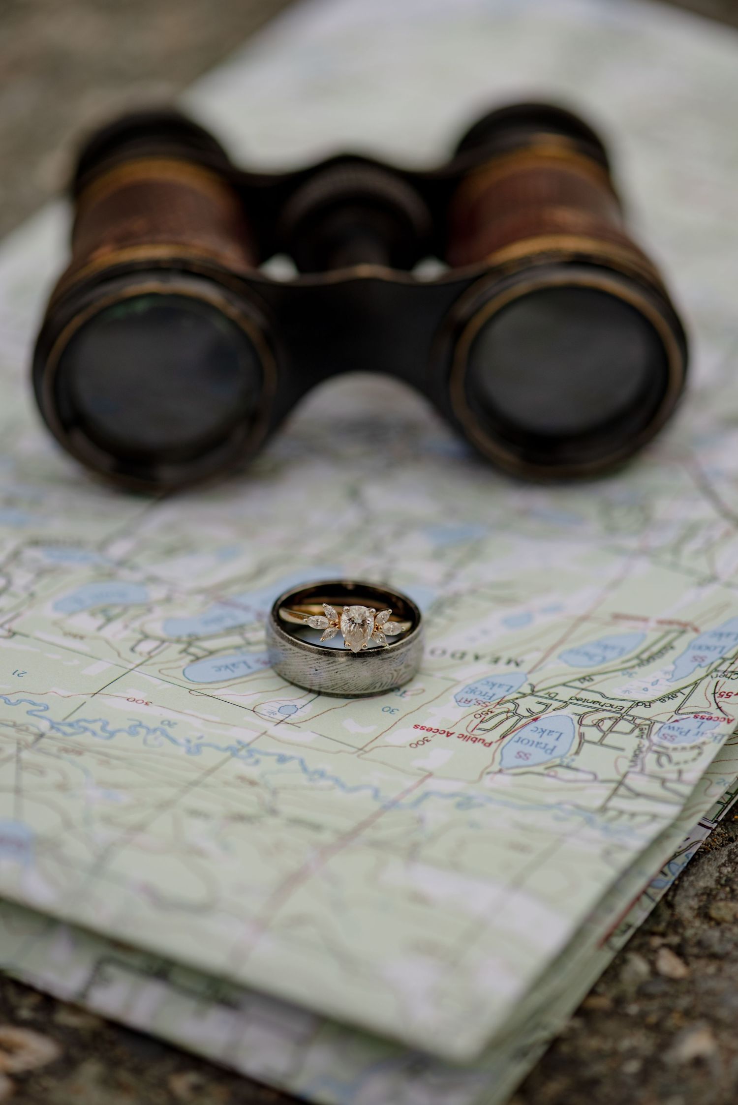 Vintage brass binoculars resting on a map beside wedding rings in a compass lid, perfect for an adventure-themed wedding.